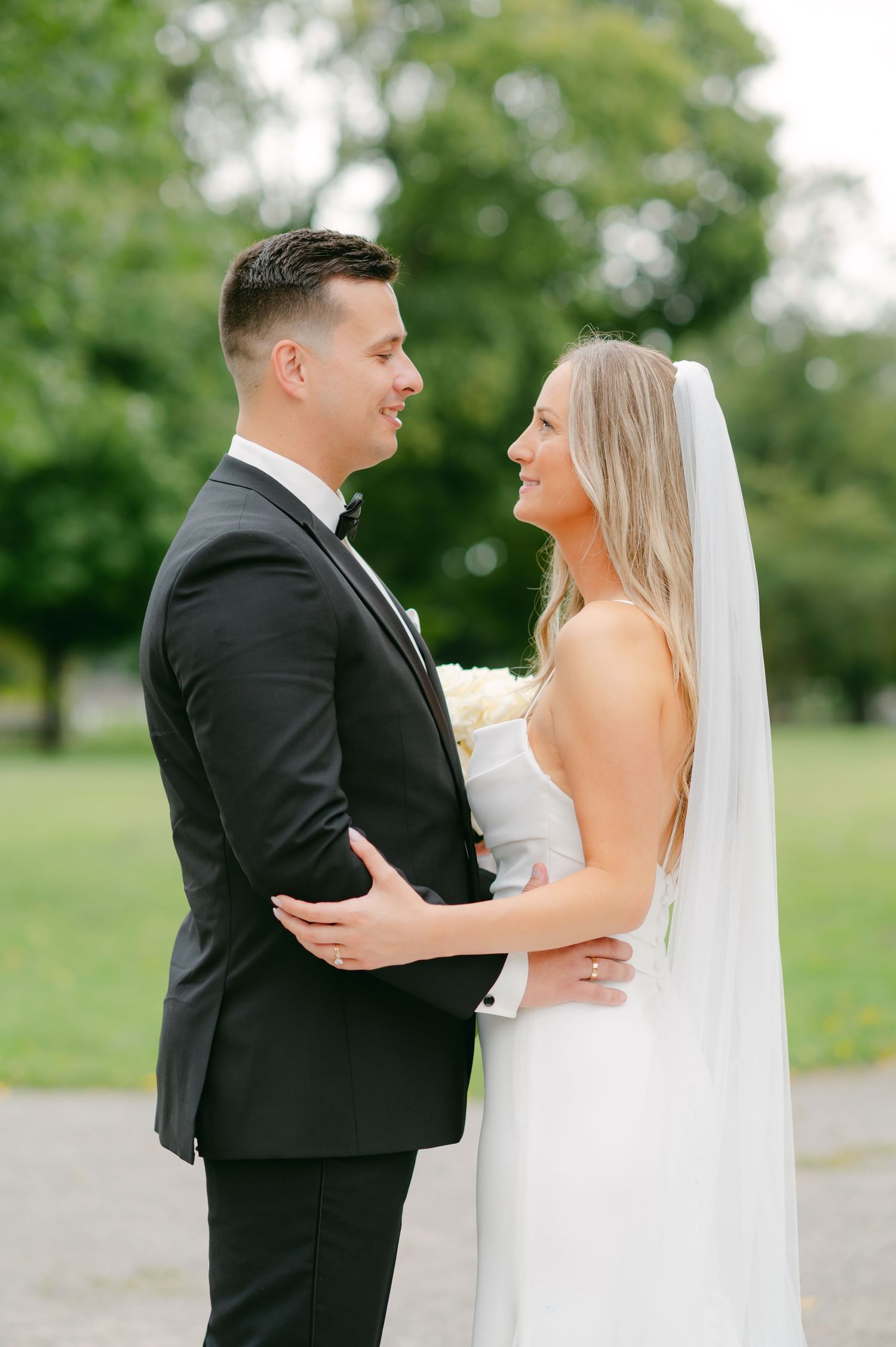 An elegant couple in wedding attire shares an intimate moment in a garden setting.