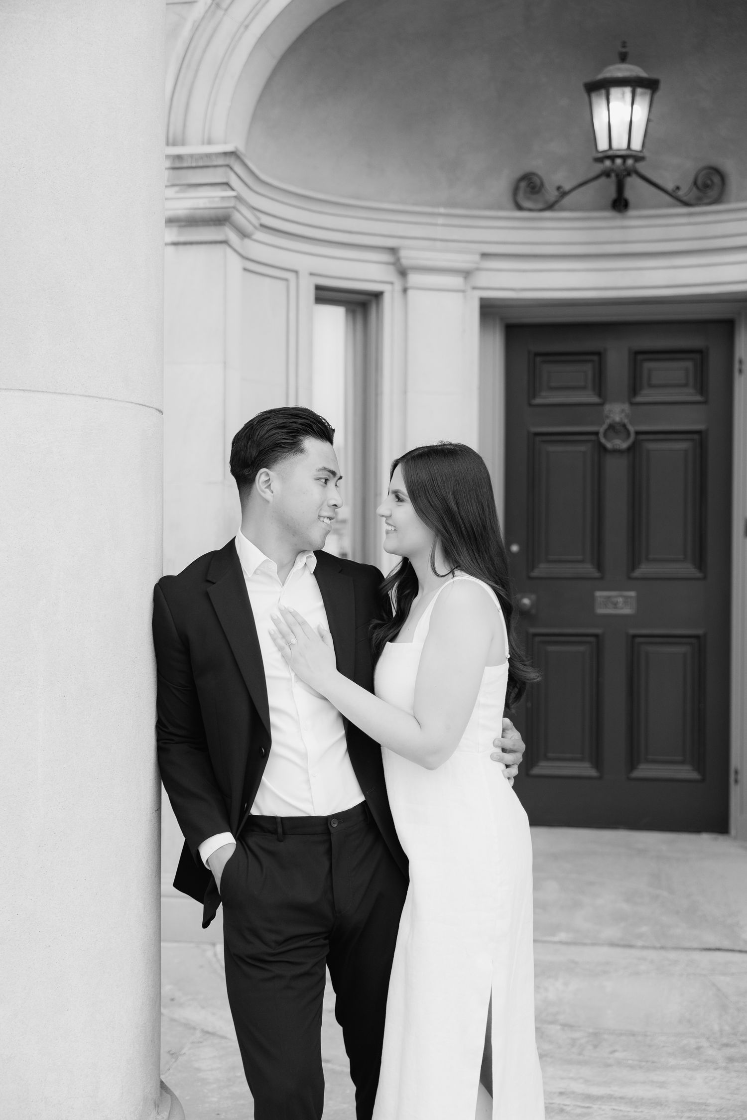 Black and white portrait of couple in formal wear sharing intimate moment by elegant entrance.