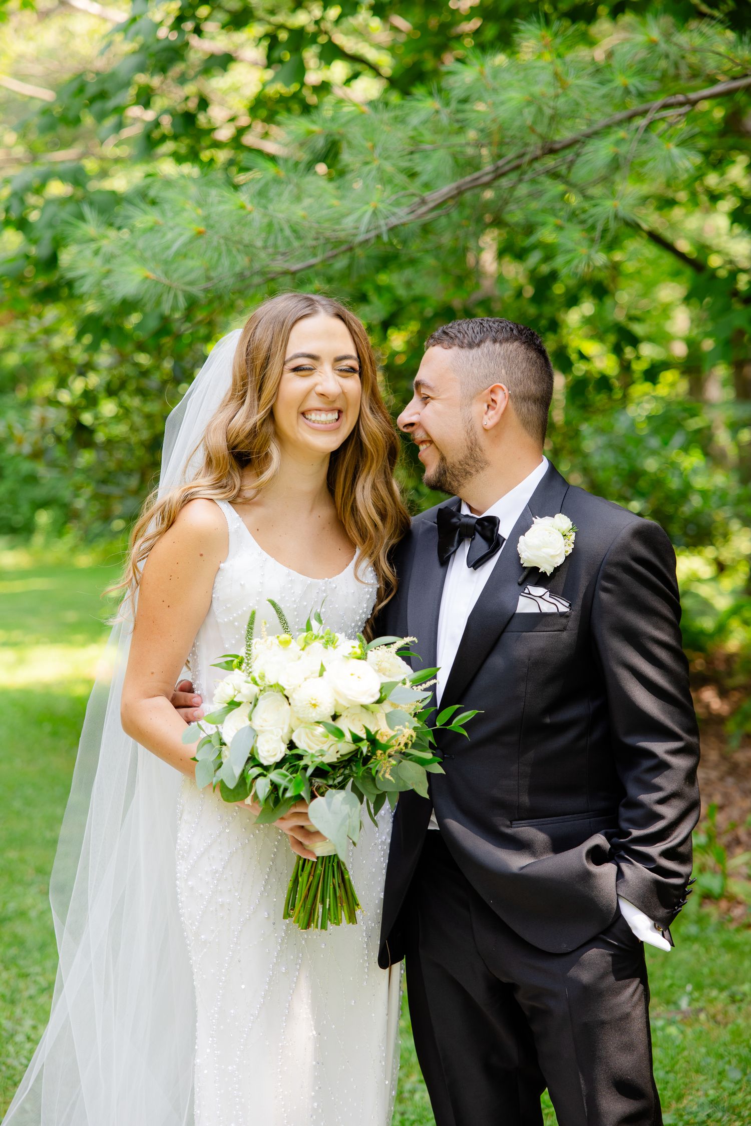 Natural light wedding portrait showing couple's joyful laughter in garden setting.