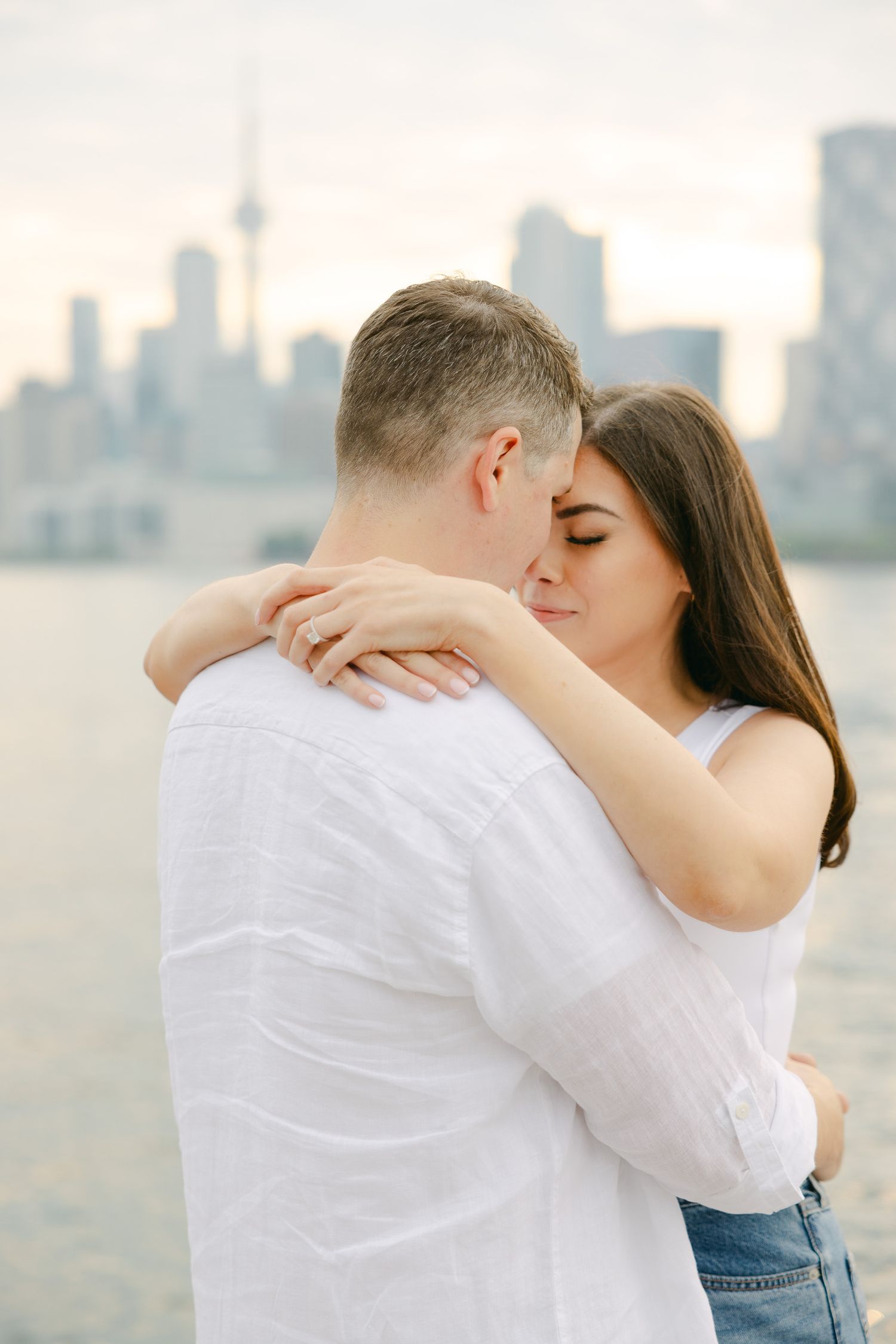 Intimate couple moment captured with Toronto cityscape in soft sunset lighting.