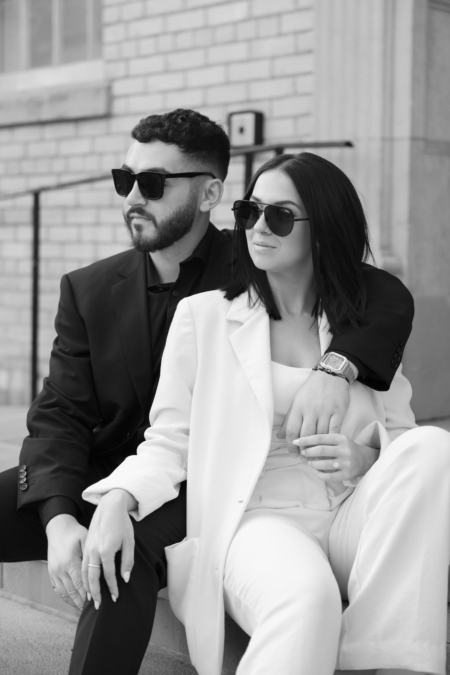 Sophisticated couple in sunglasses wearing contrasting black and white outfits pose together.