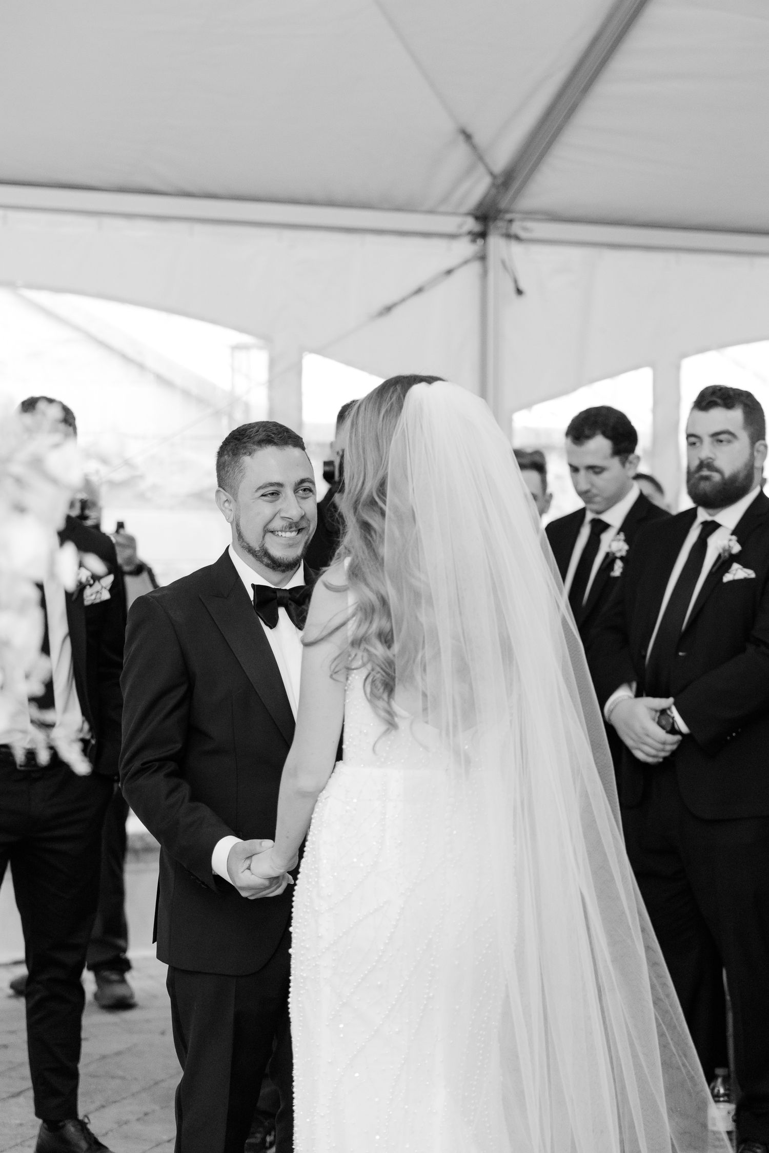Black and white wedding ceremony photo capturing emotional moment under tent.
