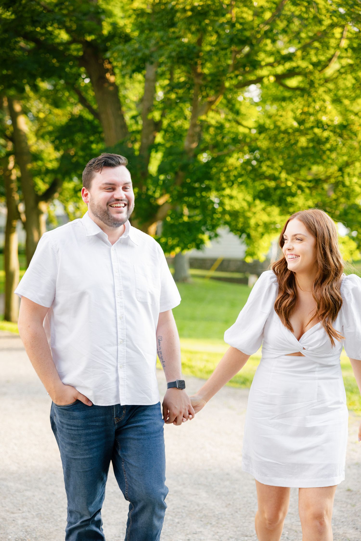 A couple laughing together while walking hand in hand on a park pathway.