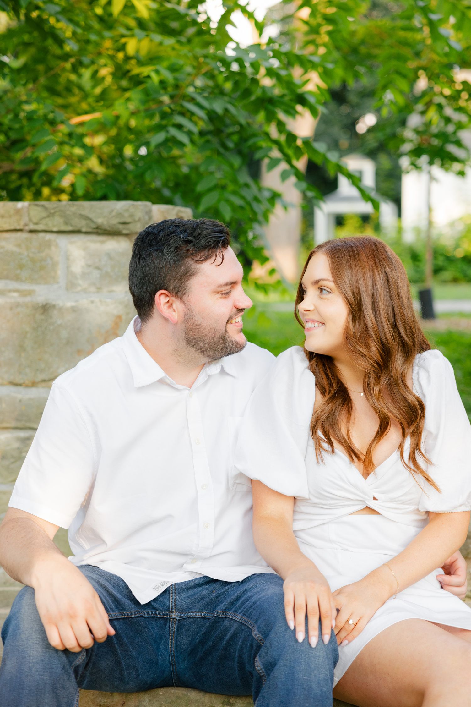 Candid moment of couple in white outfits smiling at each other on stone steps.