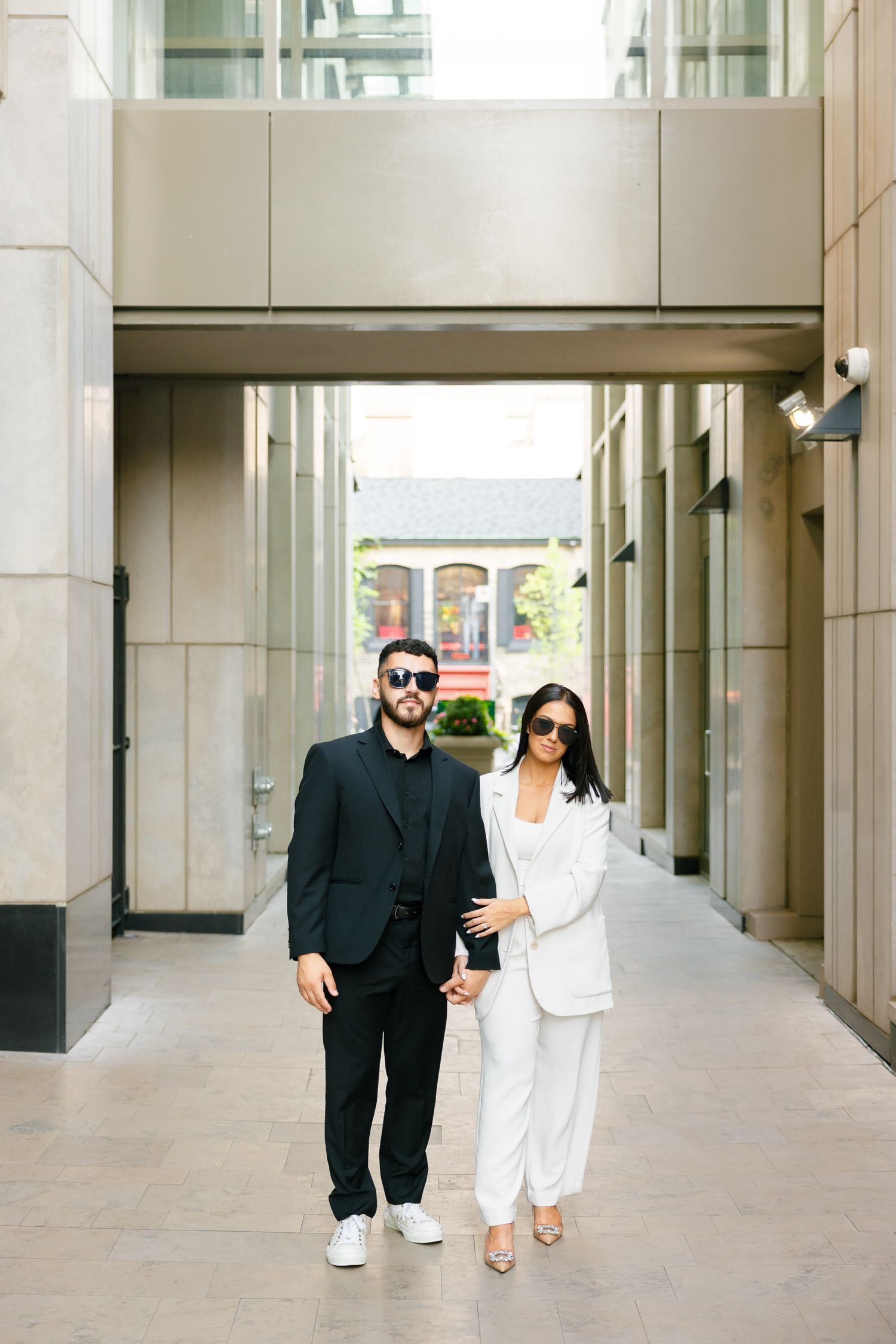 A fashionable couple walking together in a modern building corridor wearing coordinated formal outfits.