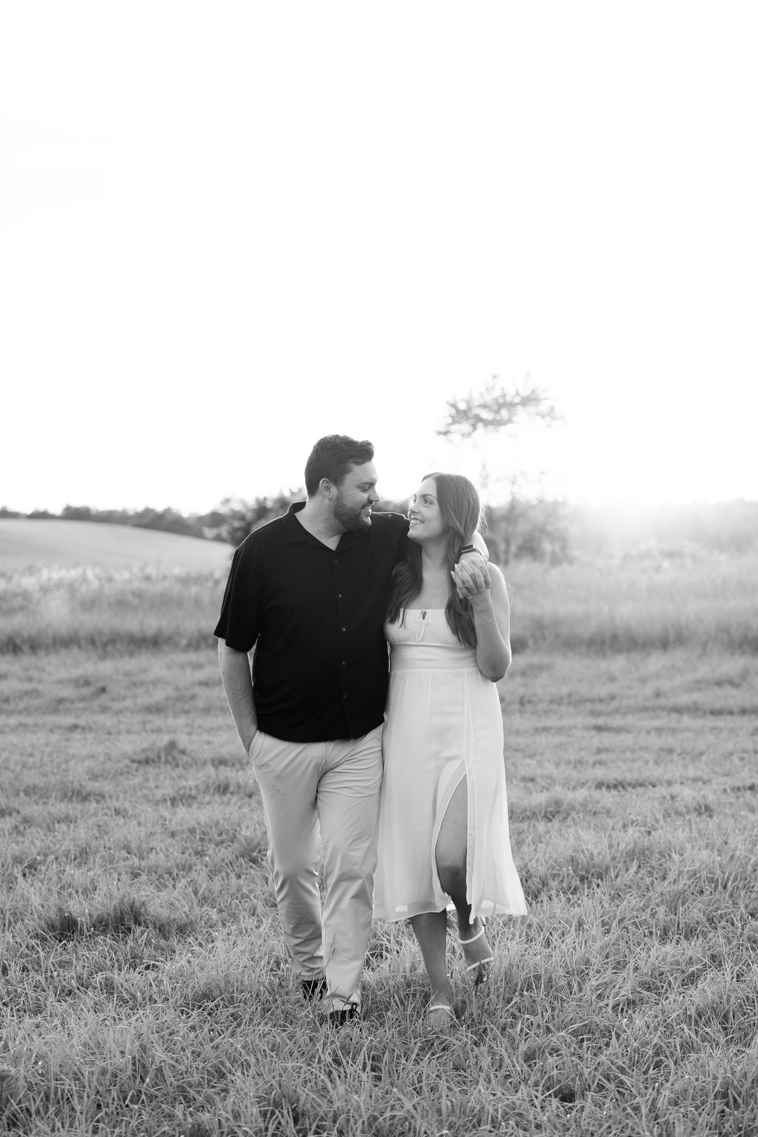 Black and white portrait of couple walking together through countryside meadow.