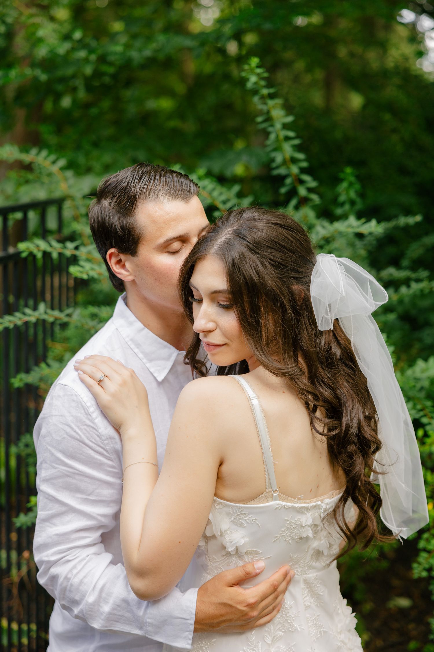 An intimate moment between a couple in wedding attire surrounded by lush greenery.