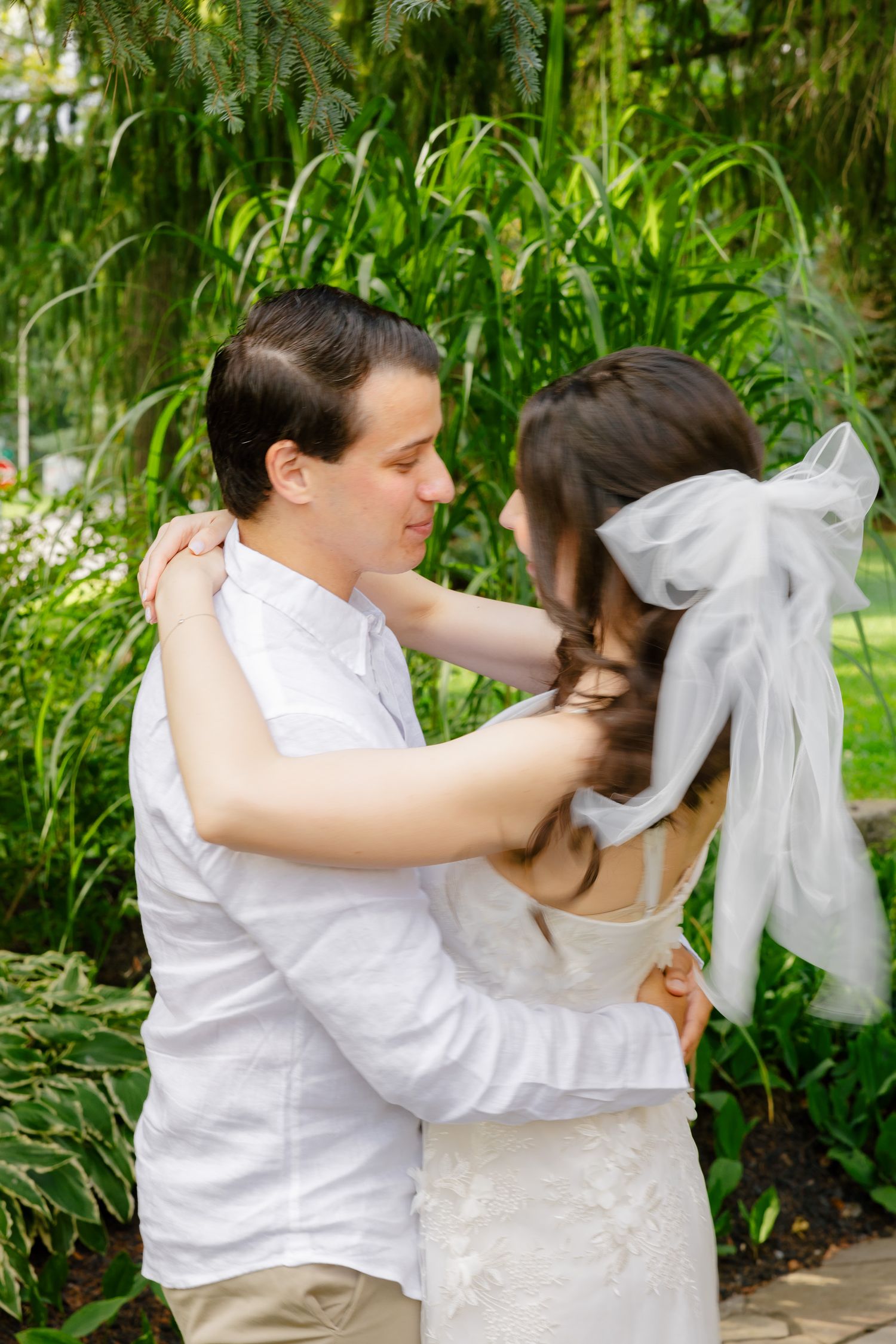 Intimate embrace between couple in wedding attire amid lush garden setting.
