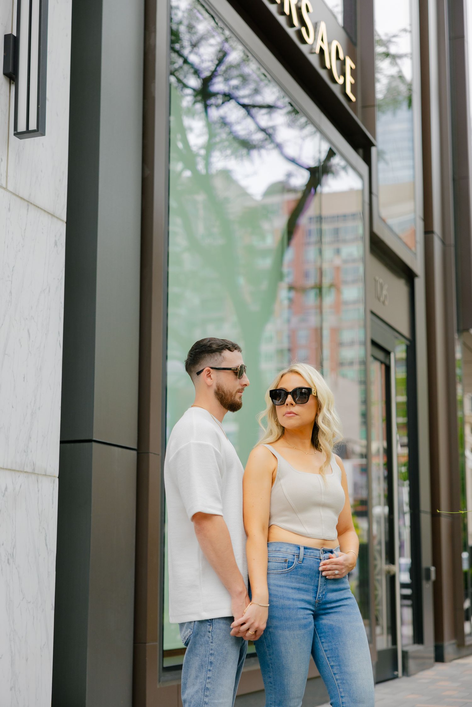 Couple in matching casual outfits standing against modern storefront wall.