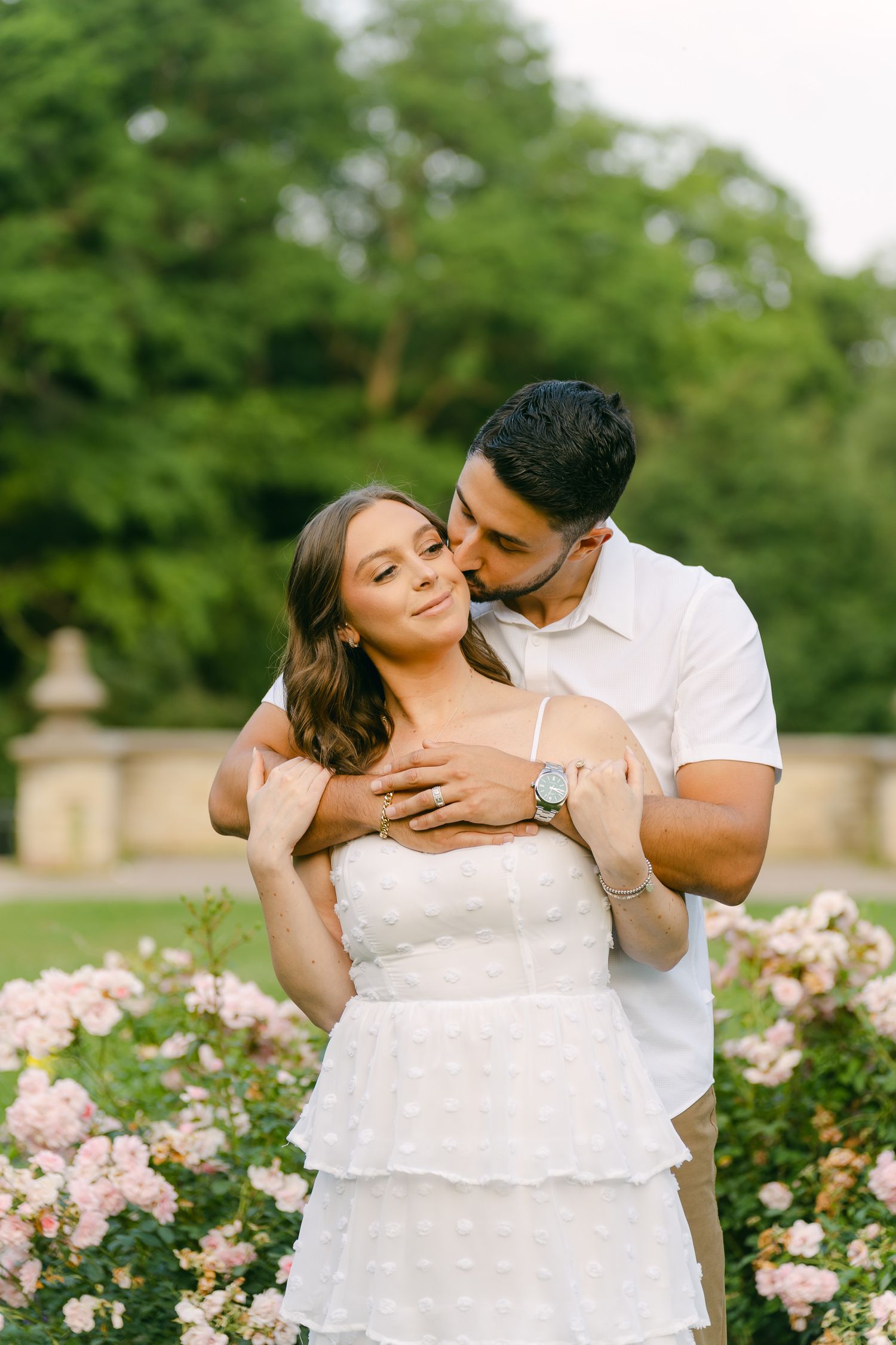 A tender moment captured between a couple in a white dress and shirt against a rose garden backdrop.