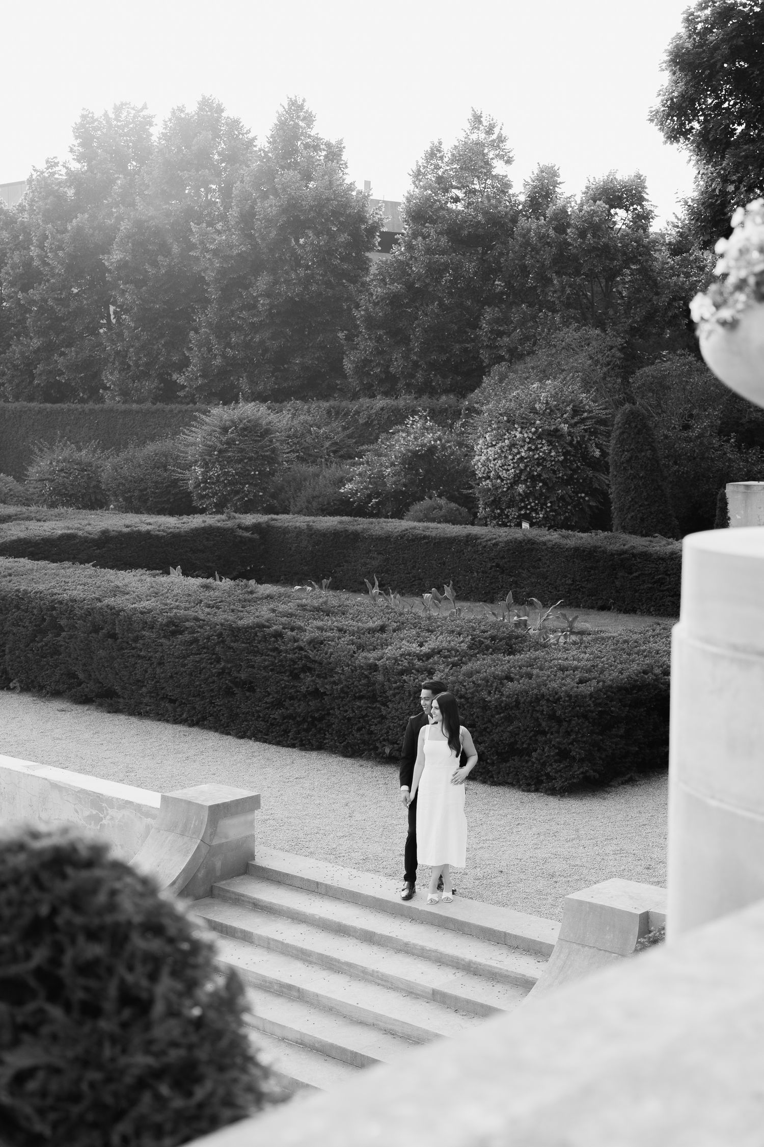 A black and white image of someone standing alone on curved stone steps in a formal garden setting.