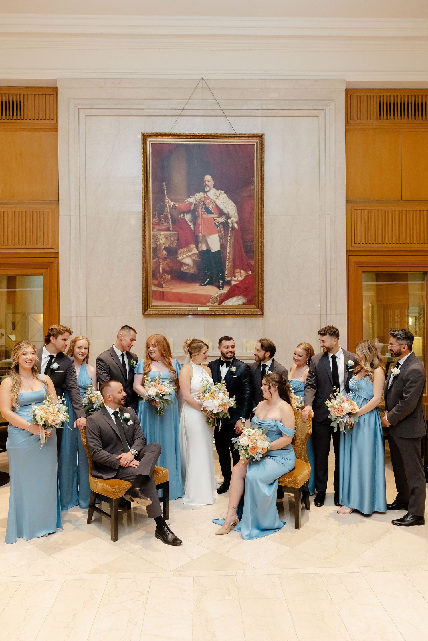Wedding party in light blue bridesmaid dresses and dark suits posed together in an elegant indoor setting.