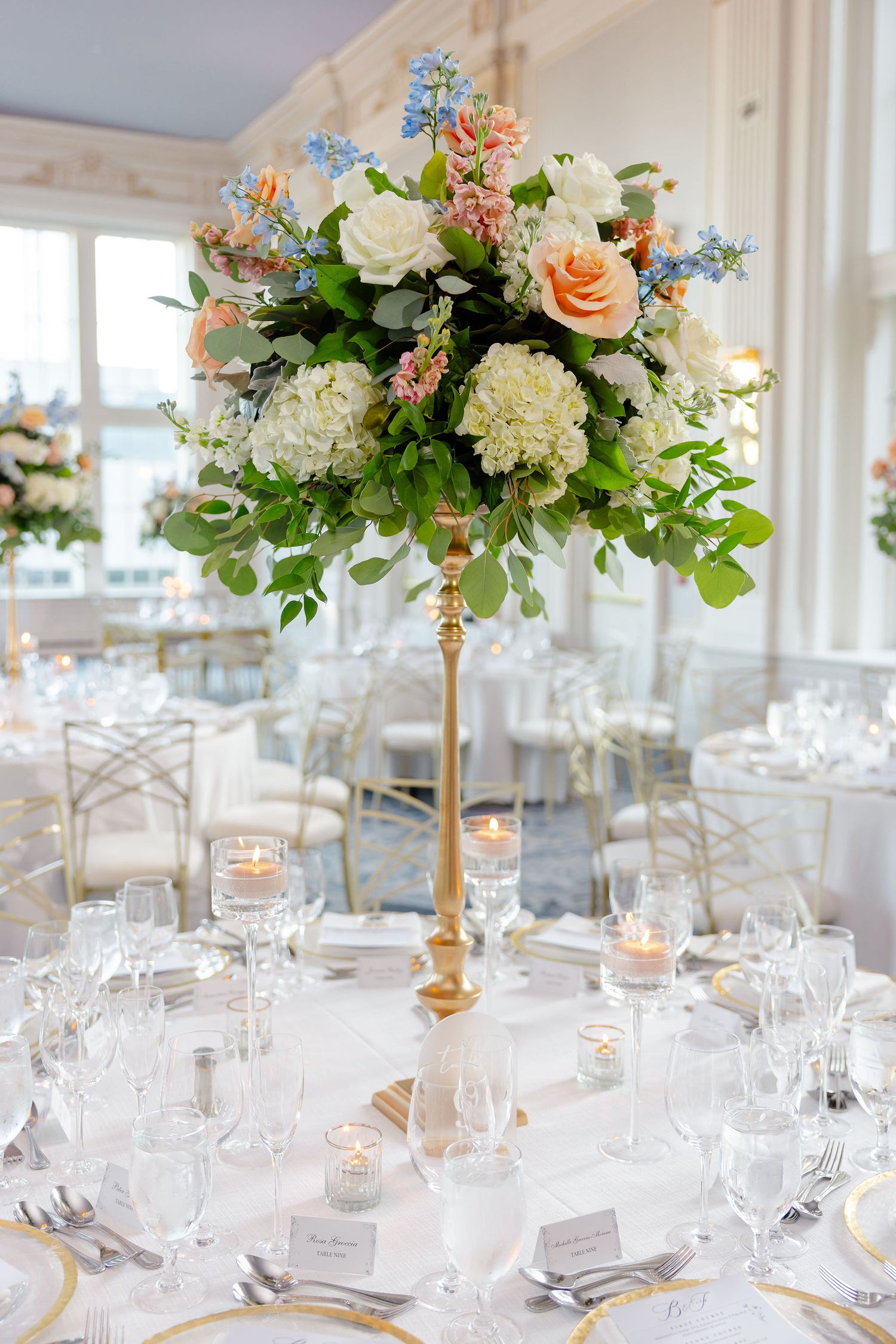 Luxurious wedding reception tables decorated with peach and white floral centerpieces on gold stands.