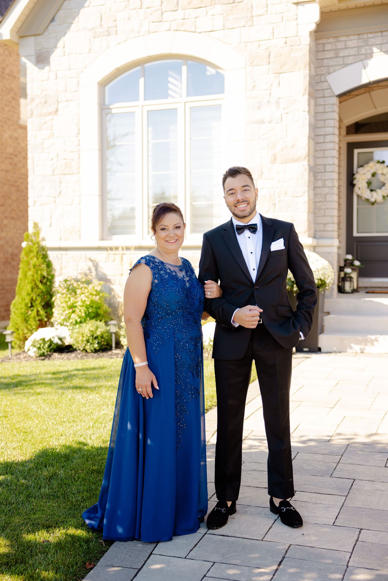 Formal couple in evening wear, a royal blue gown and black tuxedo, posing outside a stone building.
