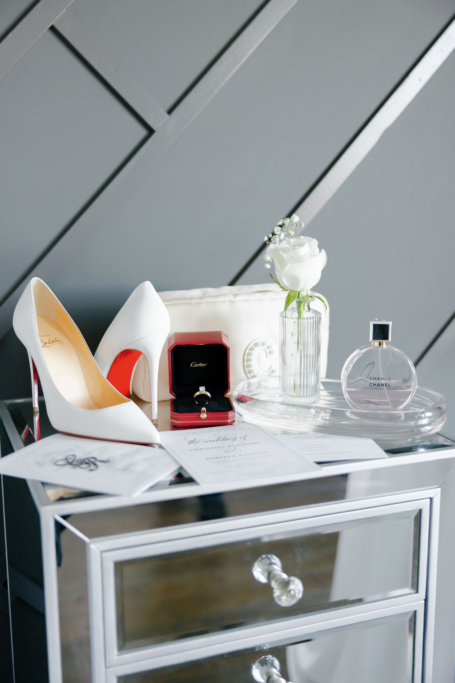 Wedding details with Cartier ring box, white heels and Chanel perfume on mirrored furniture.
