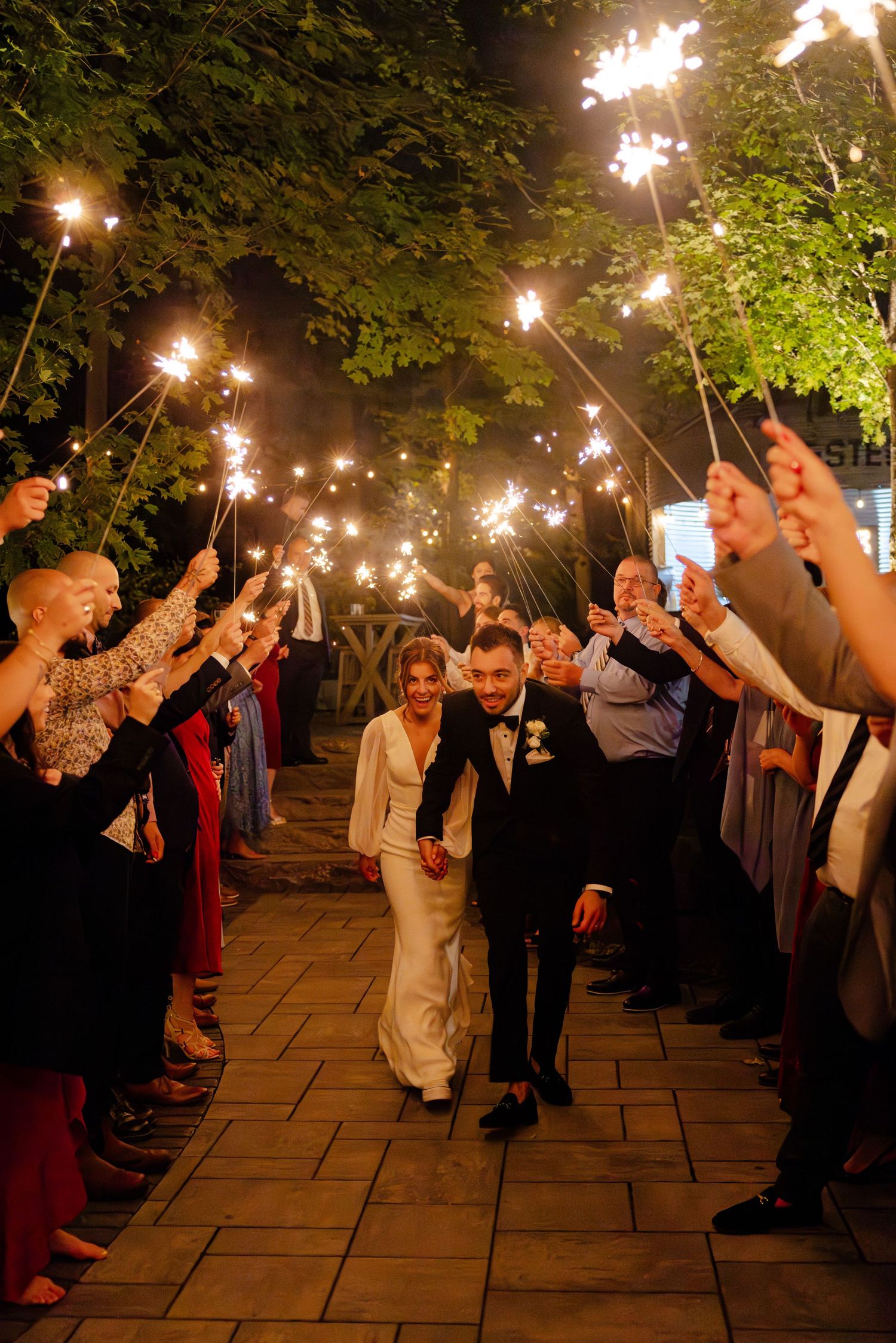 Wedding guests hold sparklers creating a luminous tunnel for a couple's grand exit.