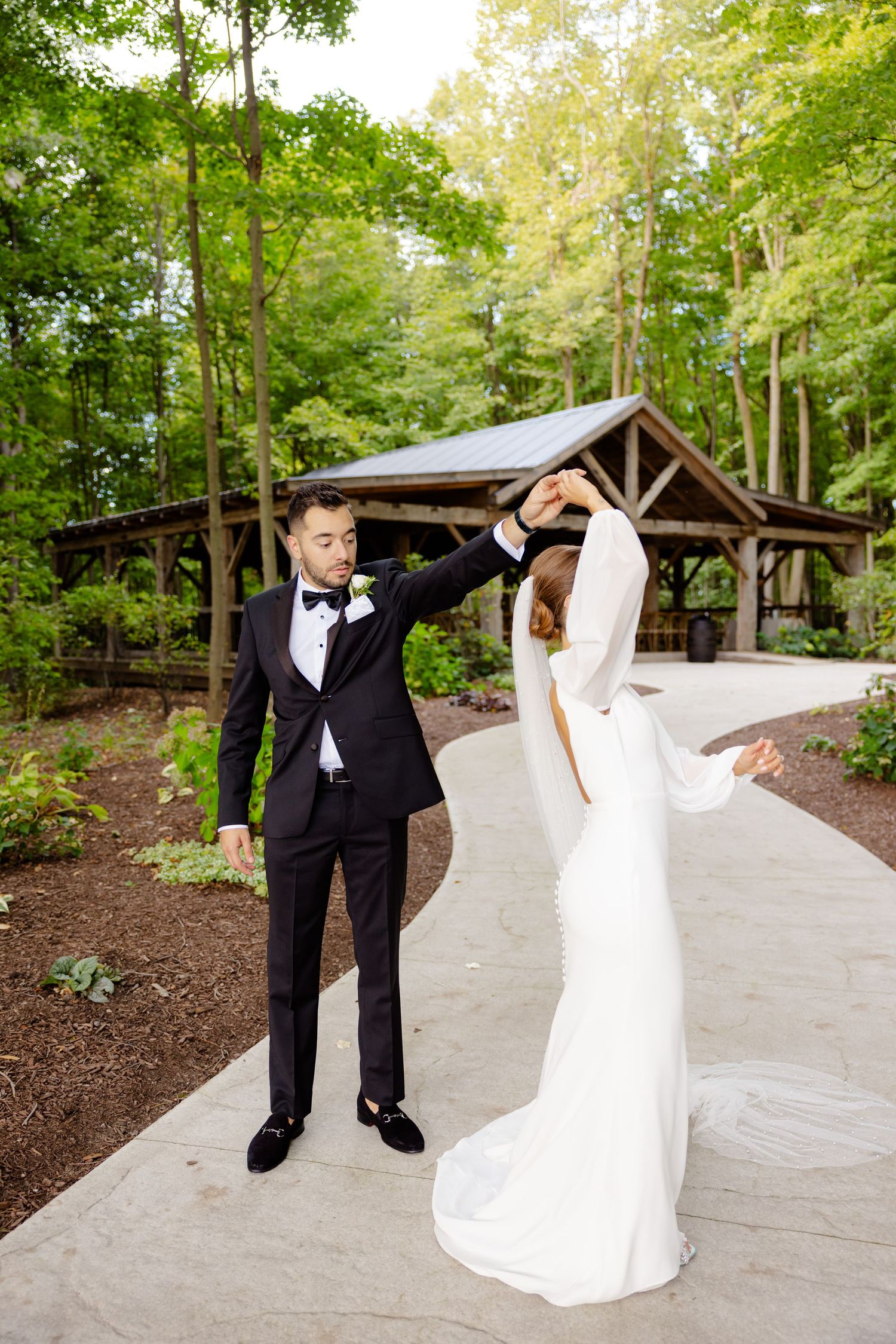 Wedding couple performs a playful dance move near a rustic forest pavilion.