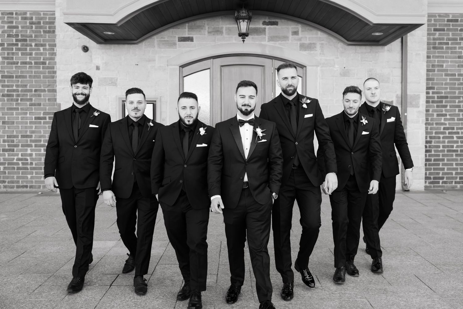 Black and white photo of groomsmen walking in formation wearing matching dark suits.
