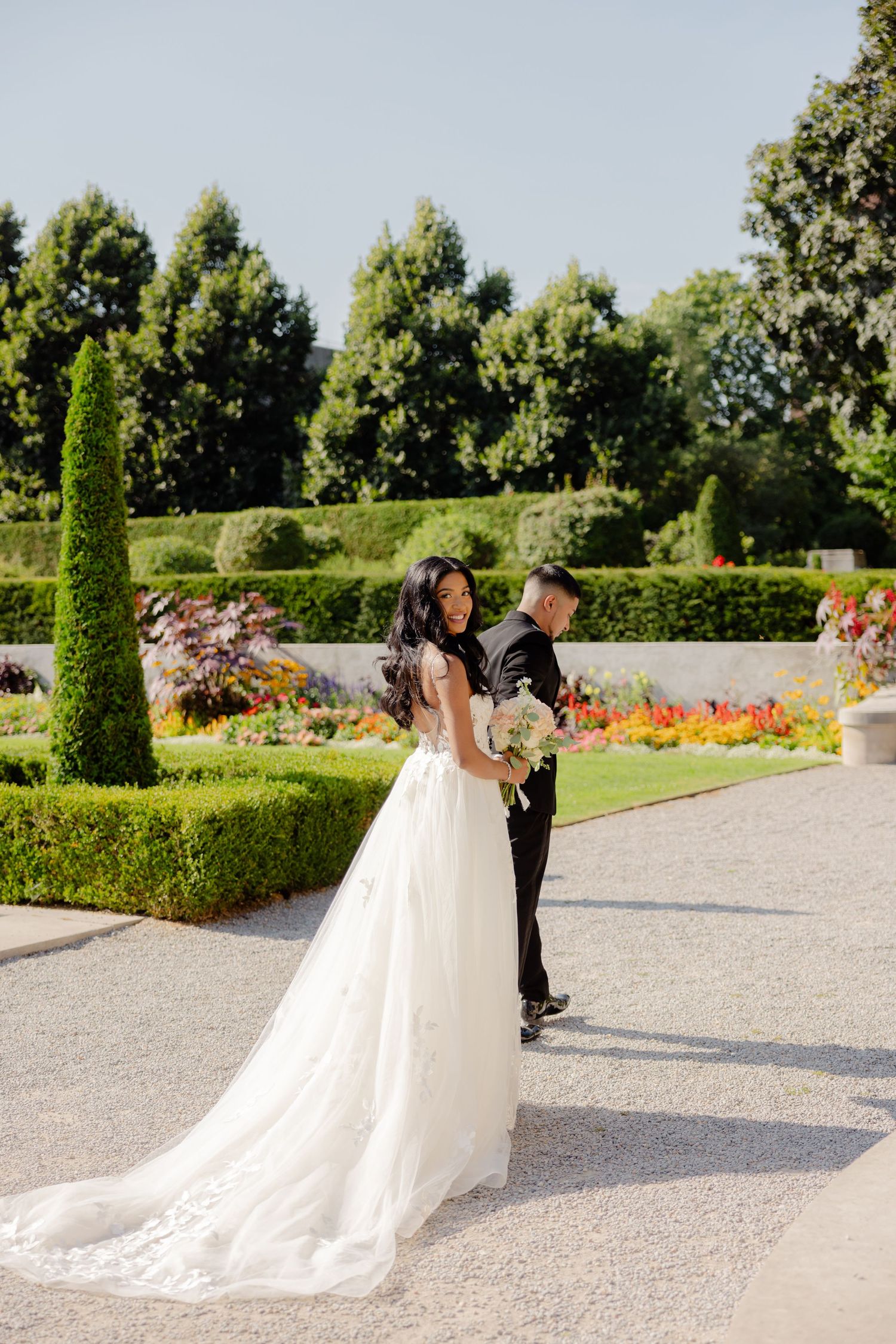 A couple embraces in a stunning garden setting with manicured hedges and colorful flowers on their wedding day.