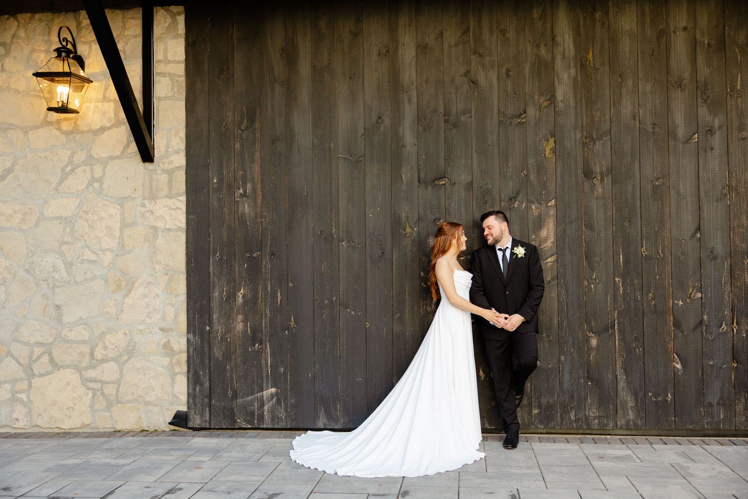 Romantic wedding portrait against weathered barn wall with vintage wall lamp.