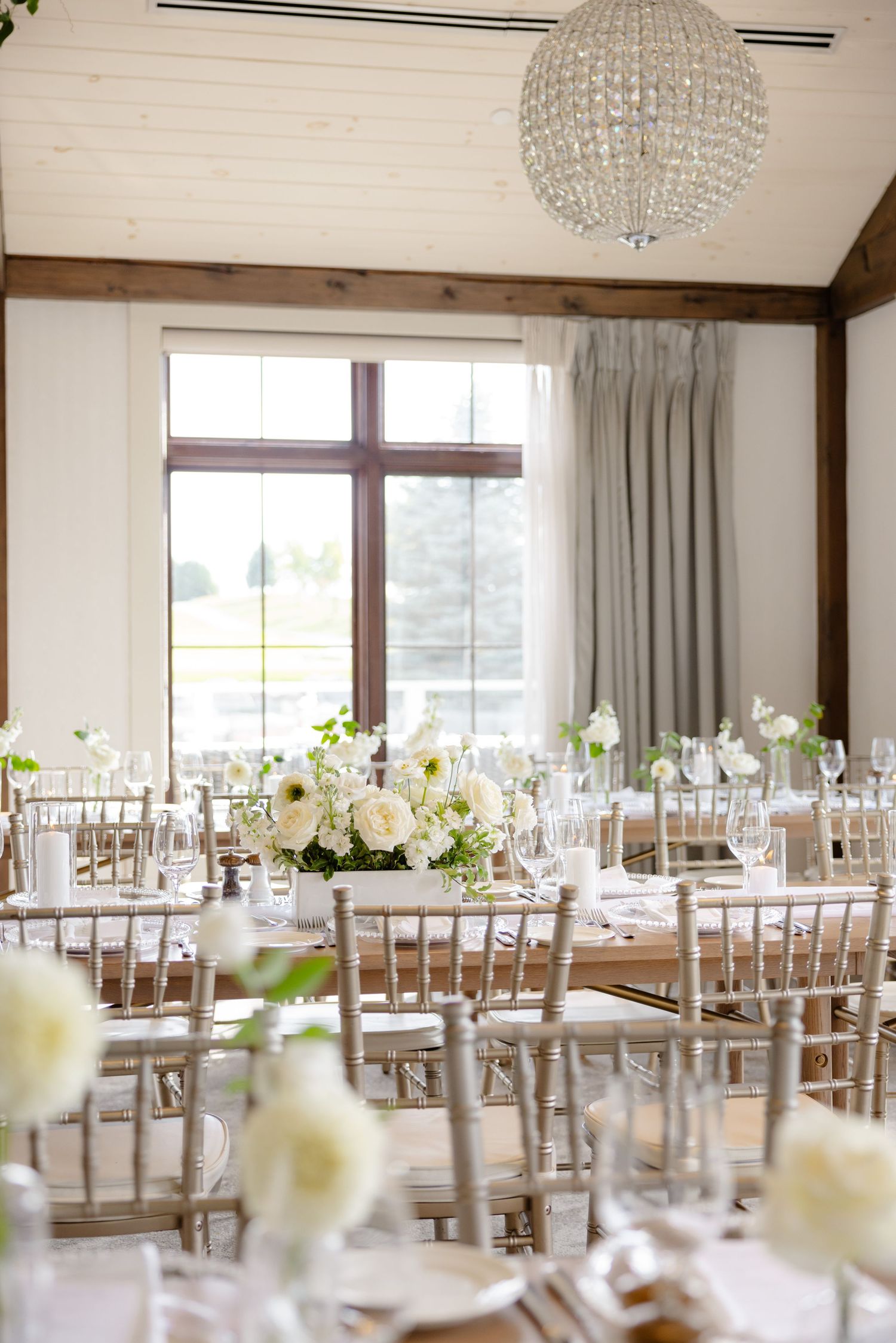 Light-filled wedding reception room with crystal chandelier and white chiavari chairs.