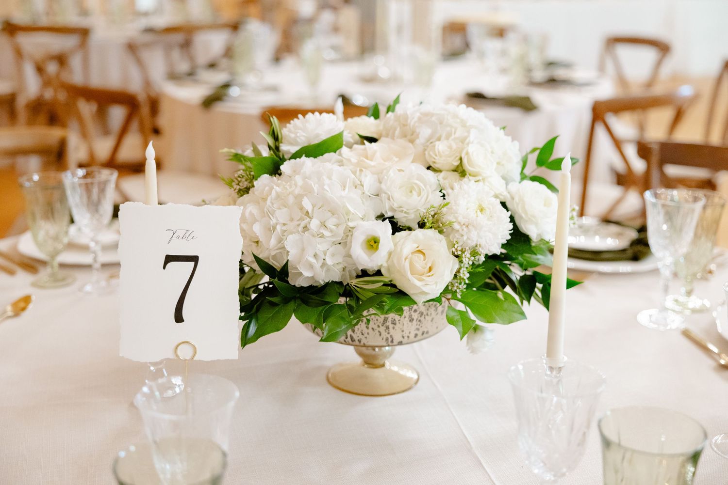 White hydrangea and rose centerpiece with table number on elegant reception table.