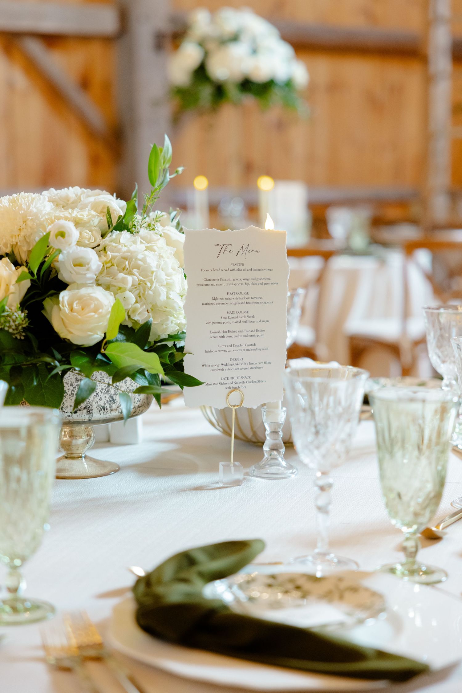 Elegant table setting with white roses, menu card, and vintage glassware in barn venue.