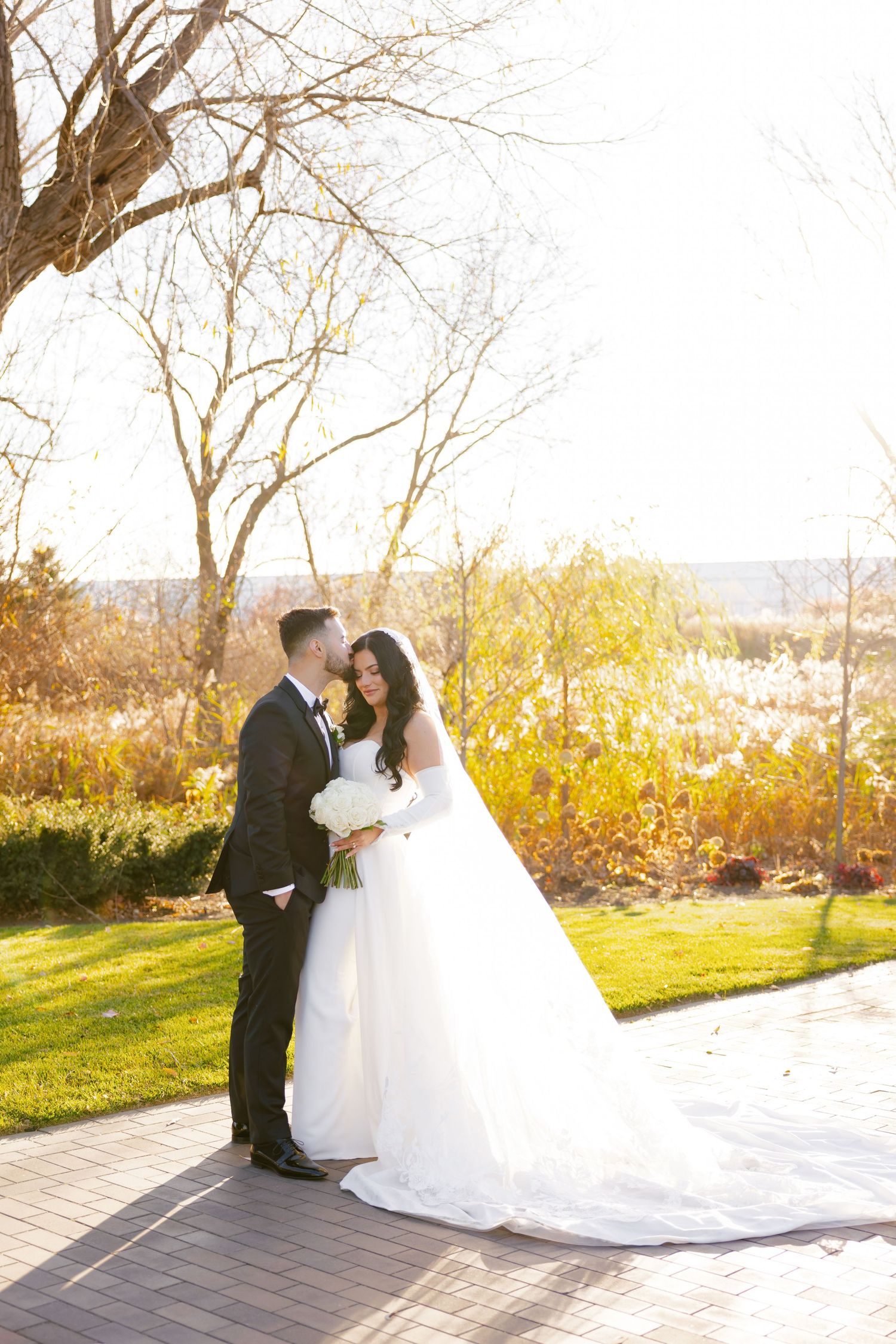 Elegant wedding portrait with bride in flowing gown against golden fall scenery.
