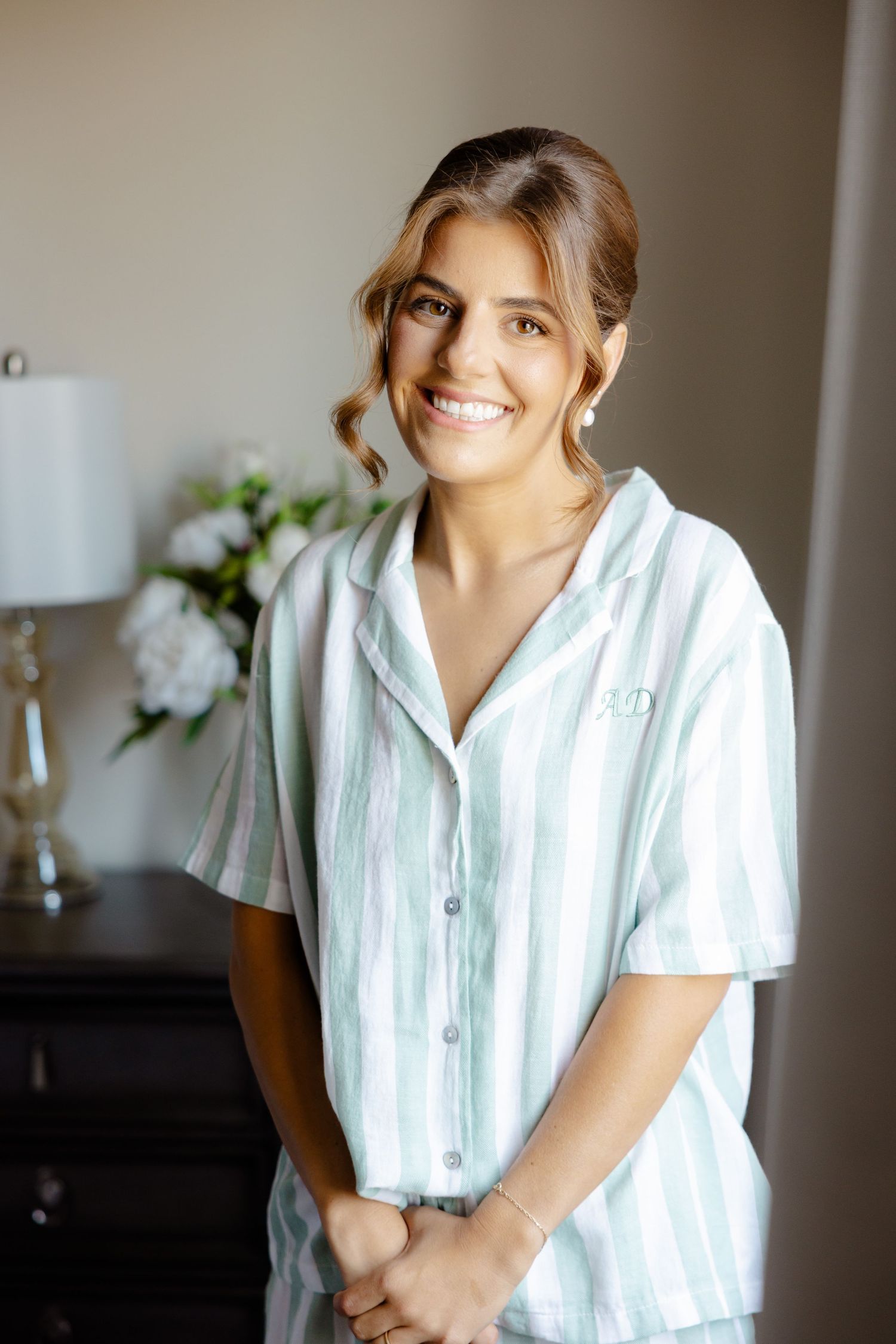 A person in a striped white pajama top smiles brightly in a bedroom setting.