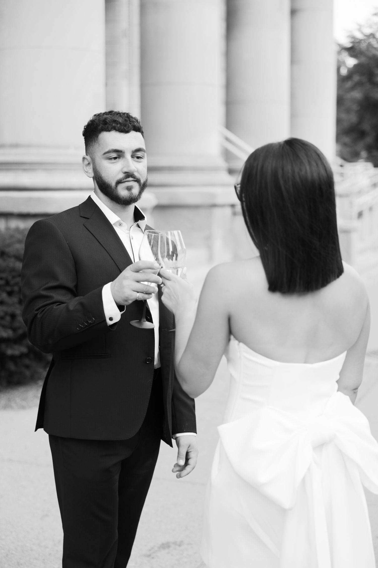Elegant pair share romantic champagne toast in formal wear by classical architecture.