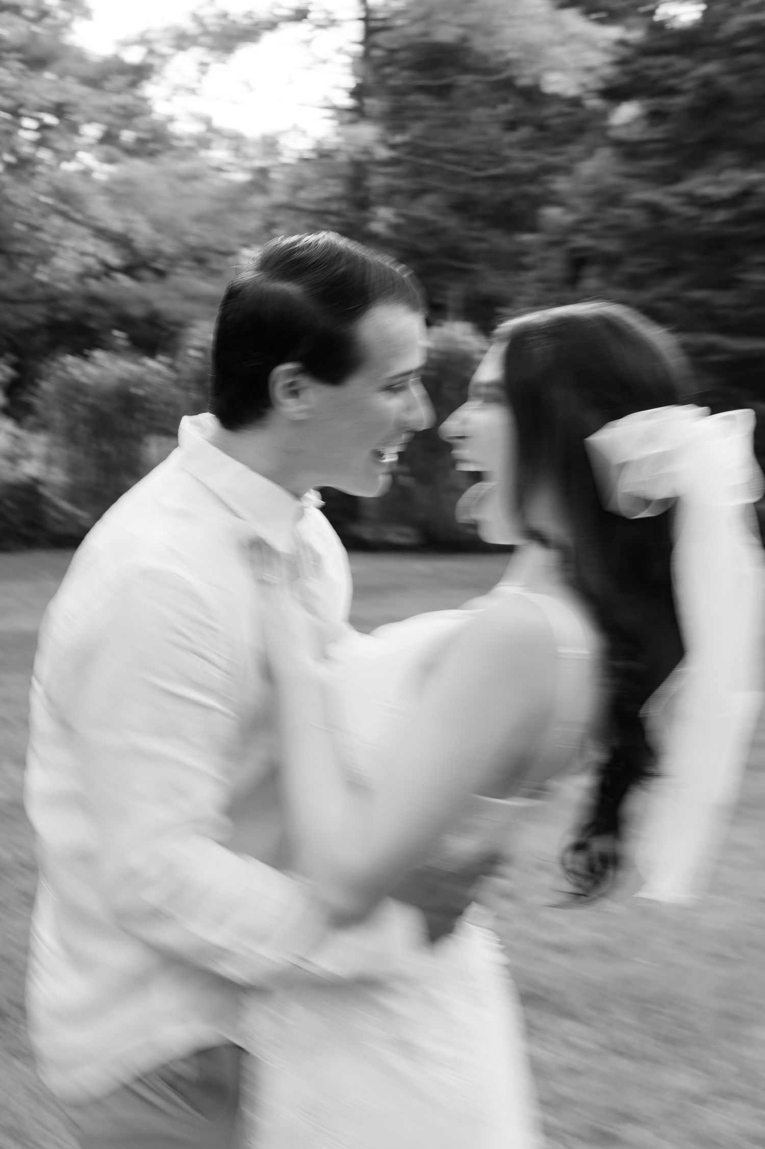 A black and white motion blur photo of a couple dancing and laughing together outdoors.