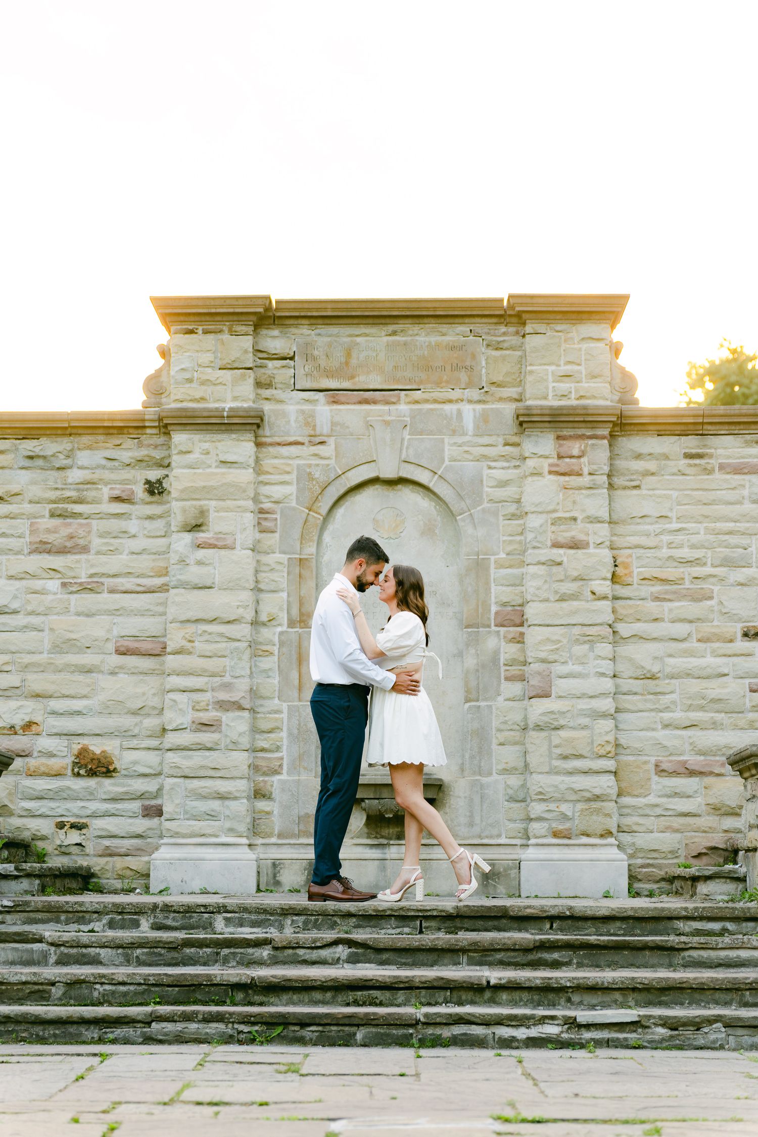 Couple embracing in stone archway on historic garden steps during sunset.