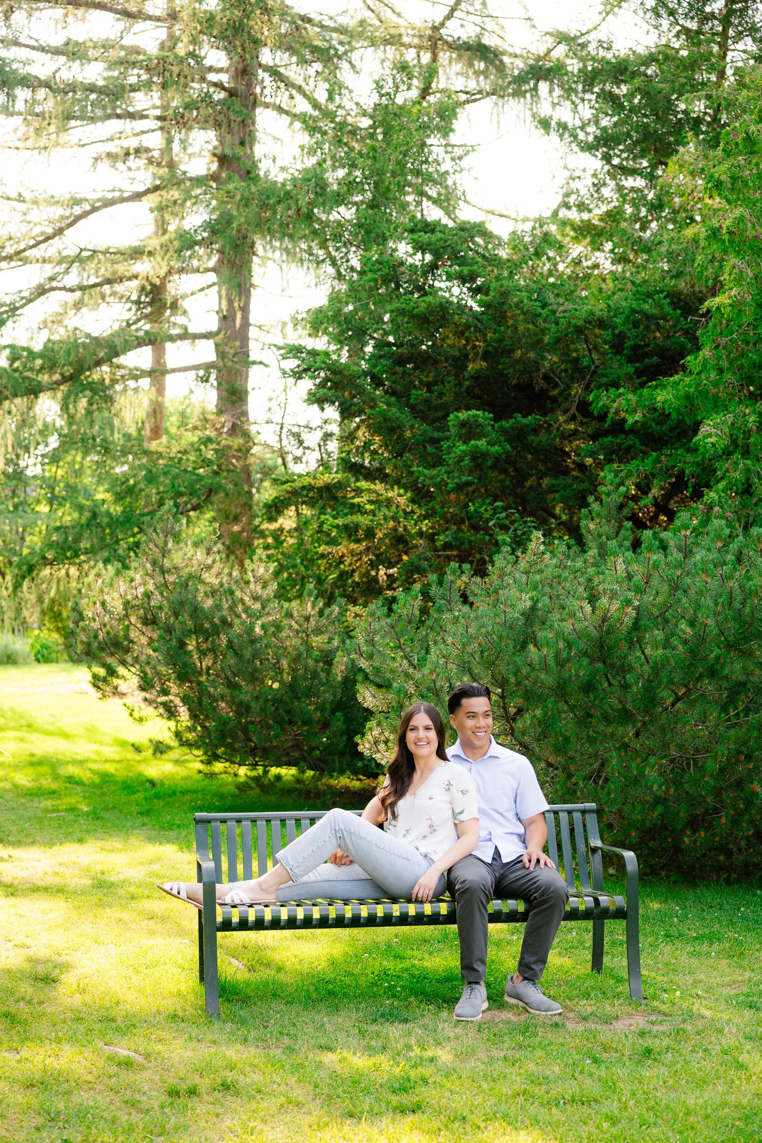 A couple enjoys a peaceful moment together on a park bench surrounded by towering evergreens.