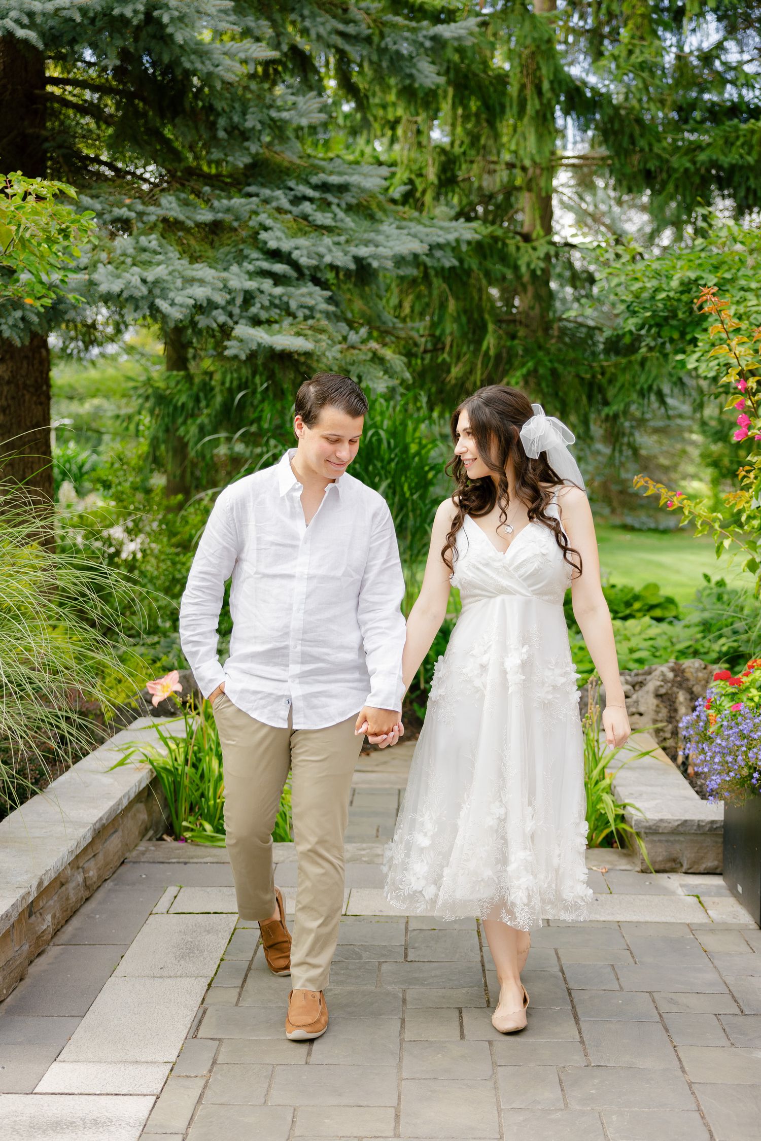 A happy couple walking hand in hand along a garden path during their wedding photoshoot.