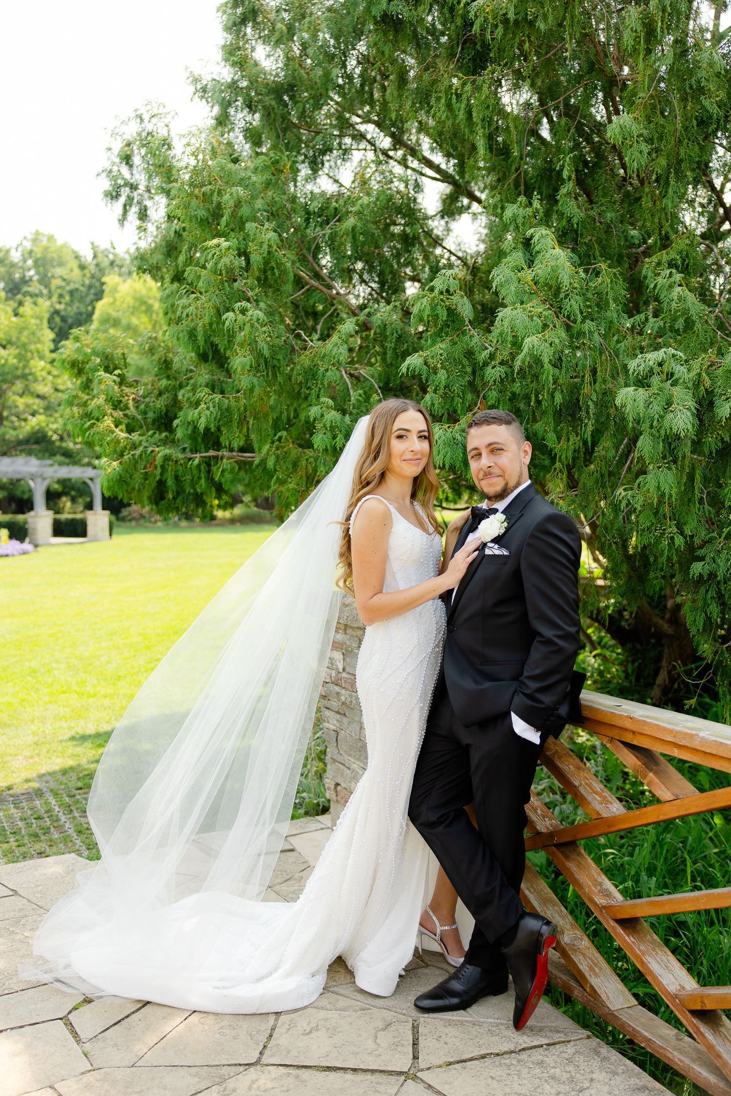 Wedding portrait against lush greenery with elegant white dress and classic tuxedo.