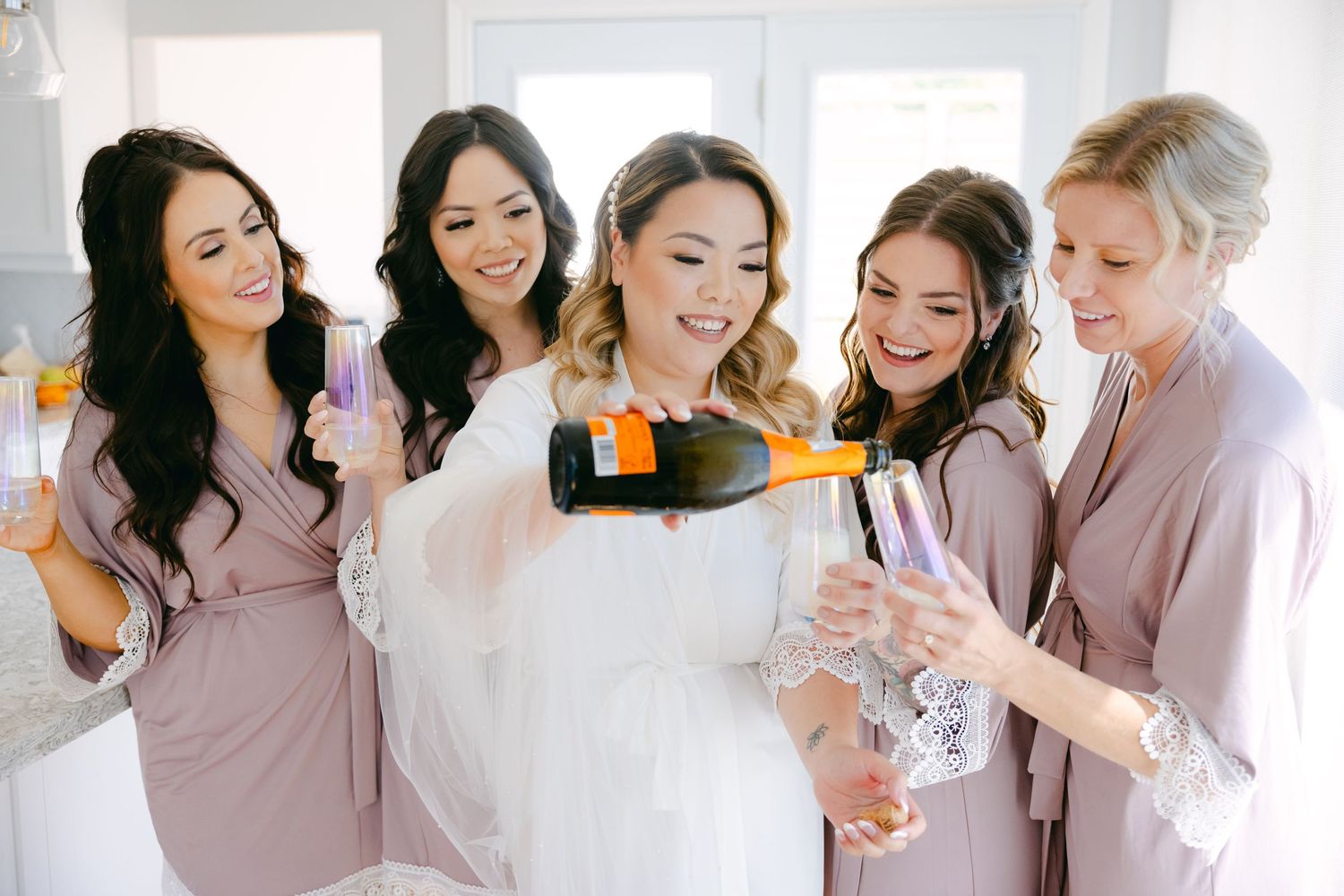 Wedding party pouring champagne and laughing together in matching robes.