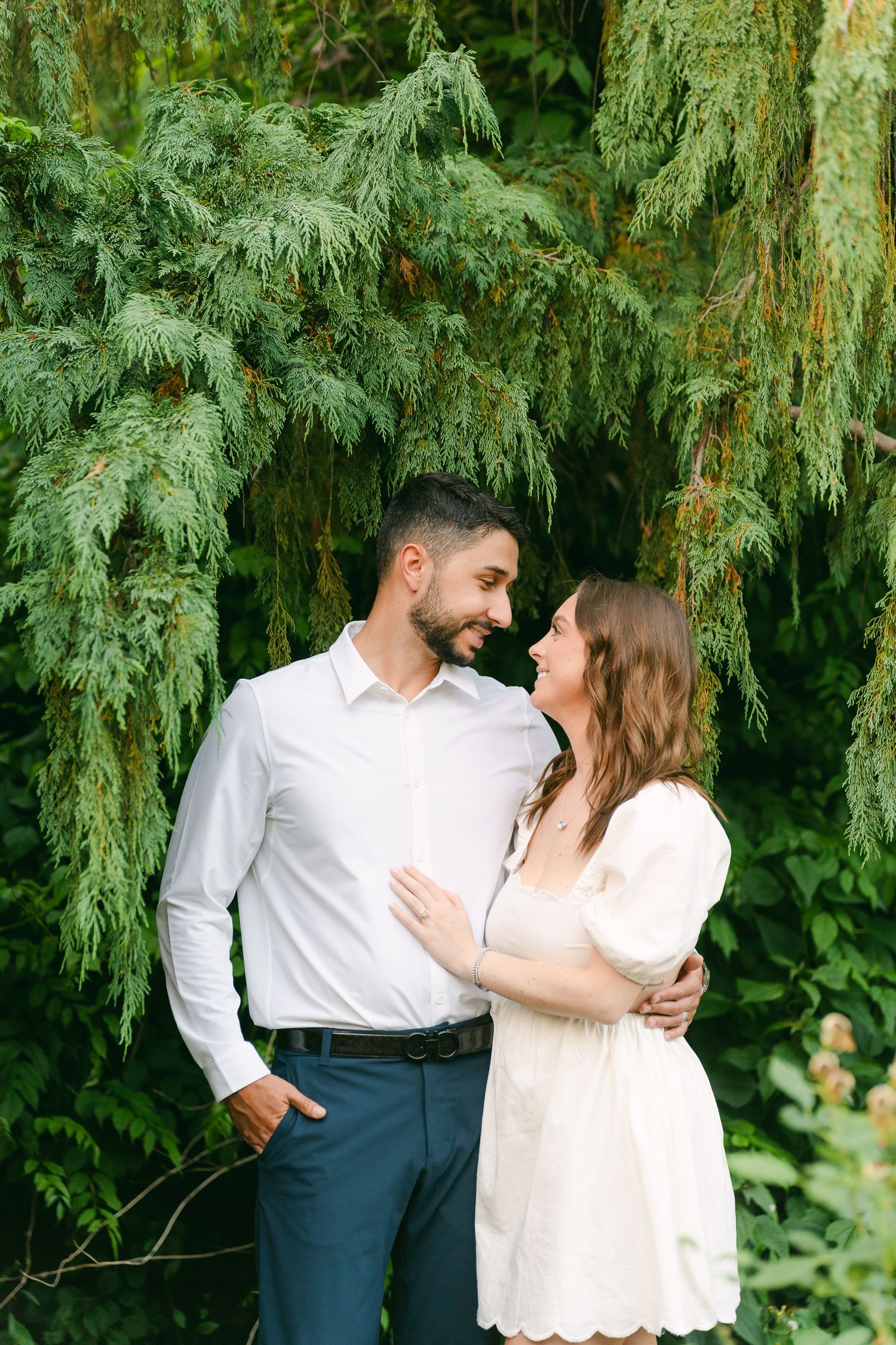 A tender moment shared between two people under a cascading willow tree in a summer garden.