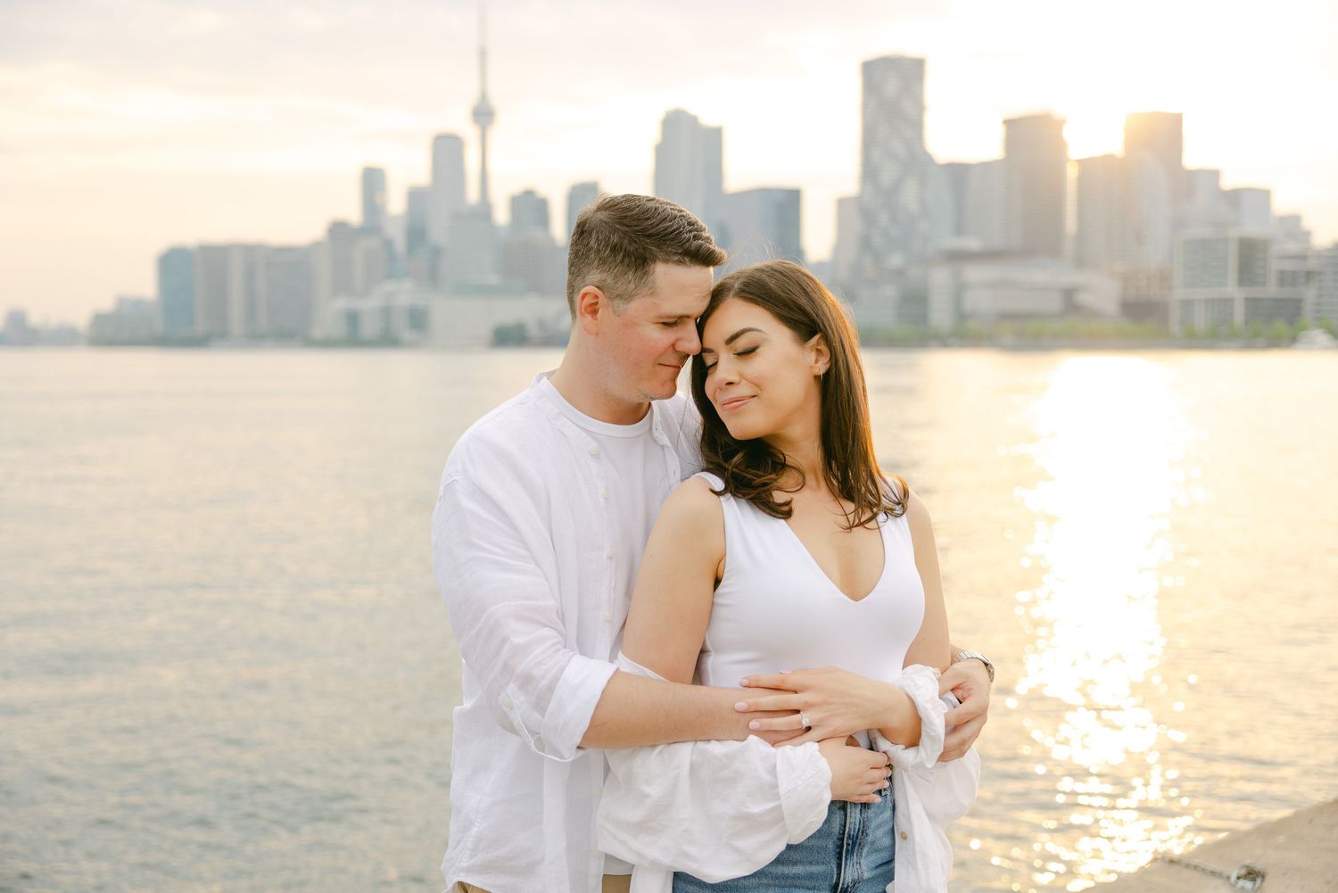 Tender moment between couple against Toronto's stunning waterfront skyline at dusk.