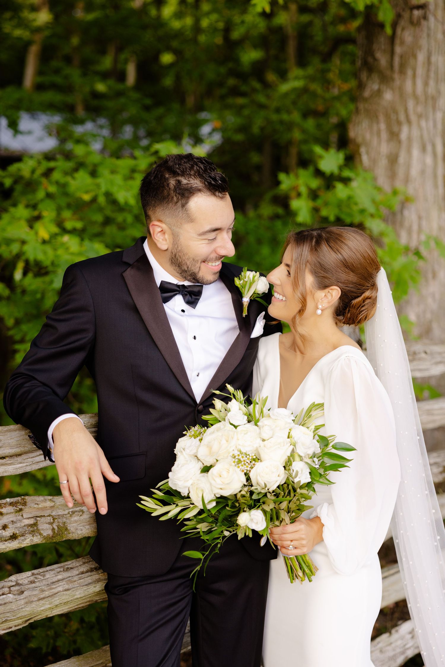 Romantic wedding couple shares a joyful moment while holding a white floral bouquet in an outdoor garden setting.