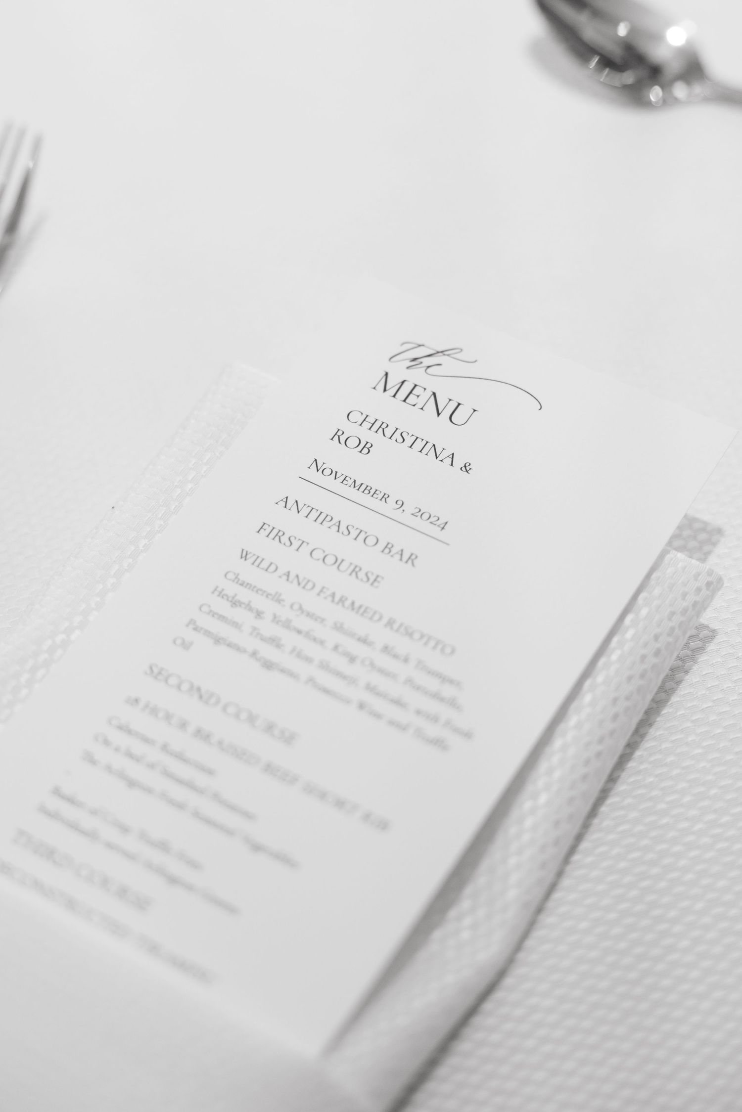 Black and white close-up of an elegant wedding menu card on a white tablecloth.