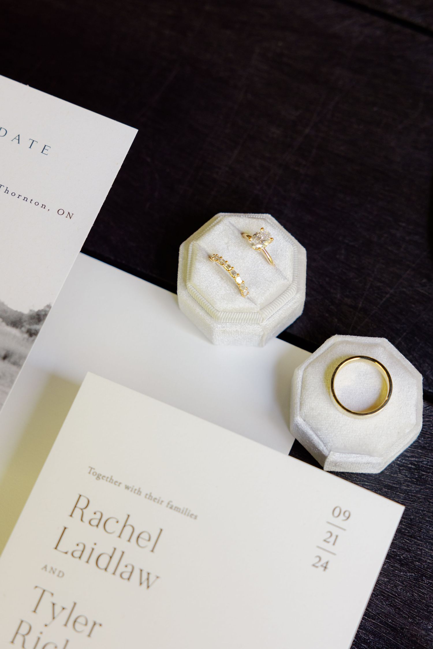 Wedding invitation with white octagonal ring boxes against dark background.