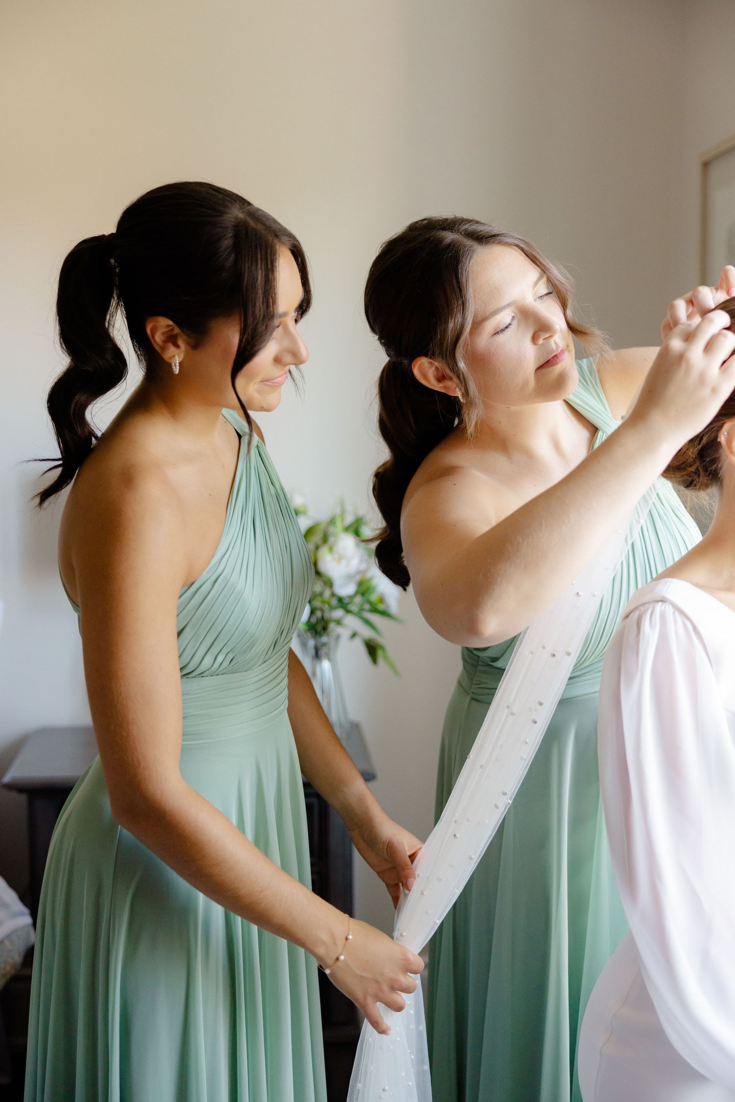Bridesmaids in mint green dresses assist with wedding preparations in natural light.