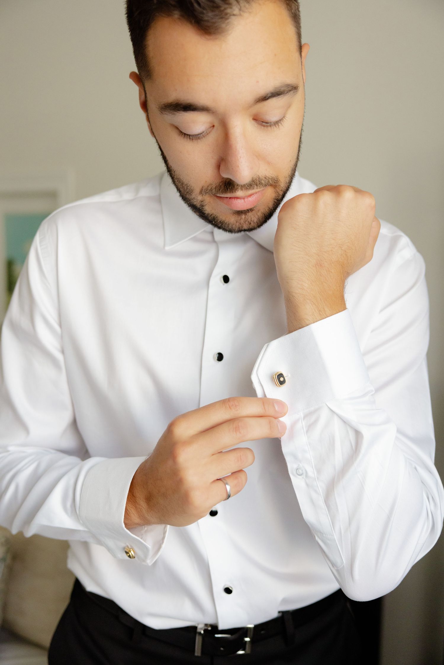 Person fastening cufflink on white dress shirt sleeve close-up.