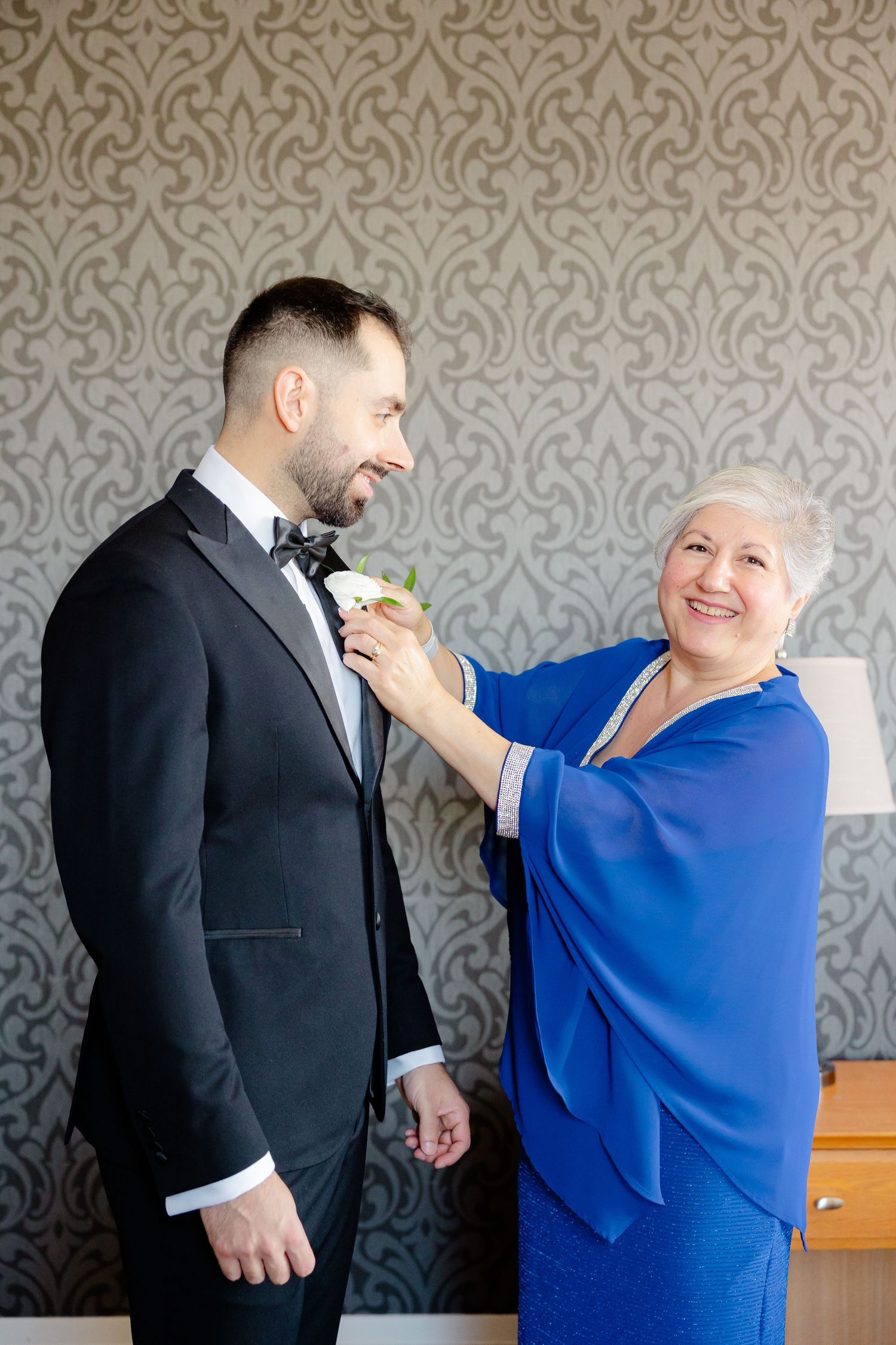A woman in royal blue adjusts a boutonniere on a person wearing a black tuxedo.