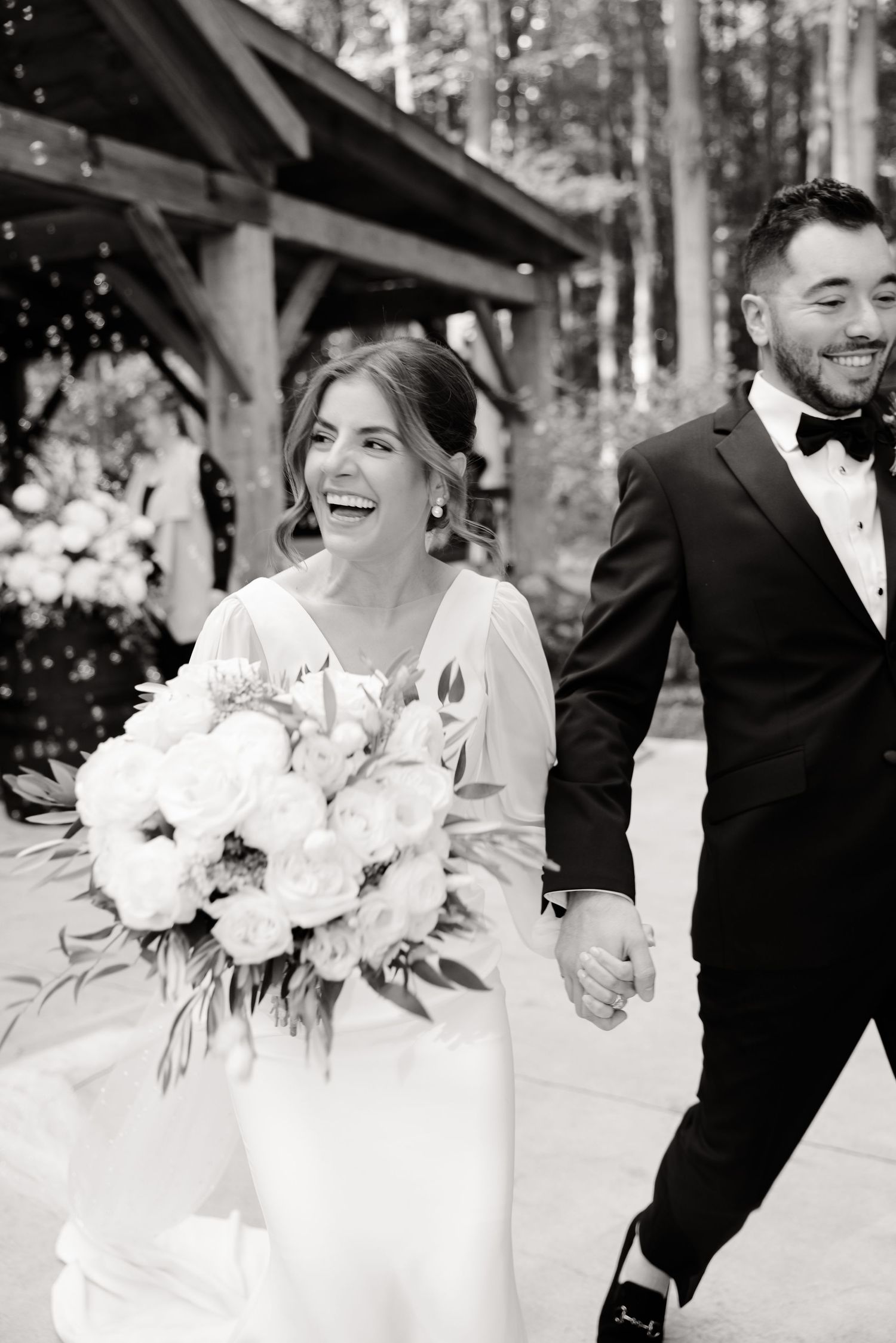 Black and white photo of newlyweds laughing together during their outdoor forest wedding celebration.