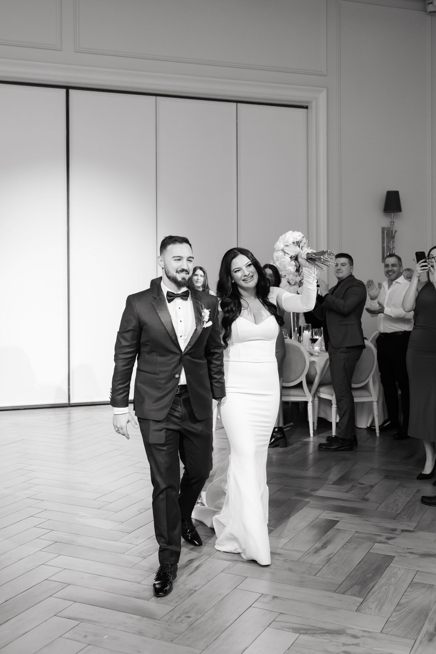 Black and white photo of newlyweds walking during wedding reception on herringbone floors.