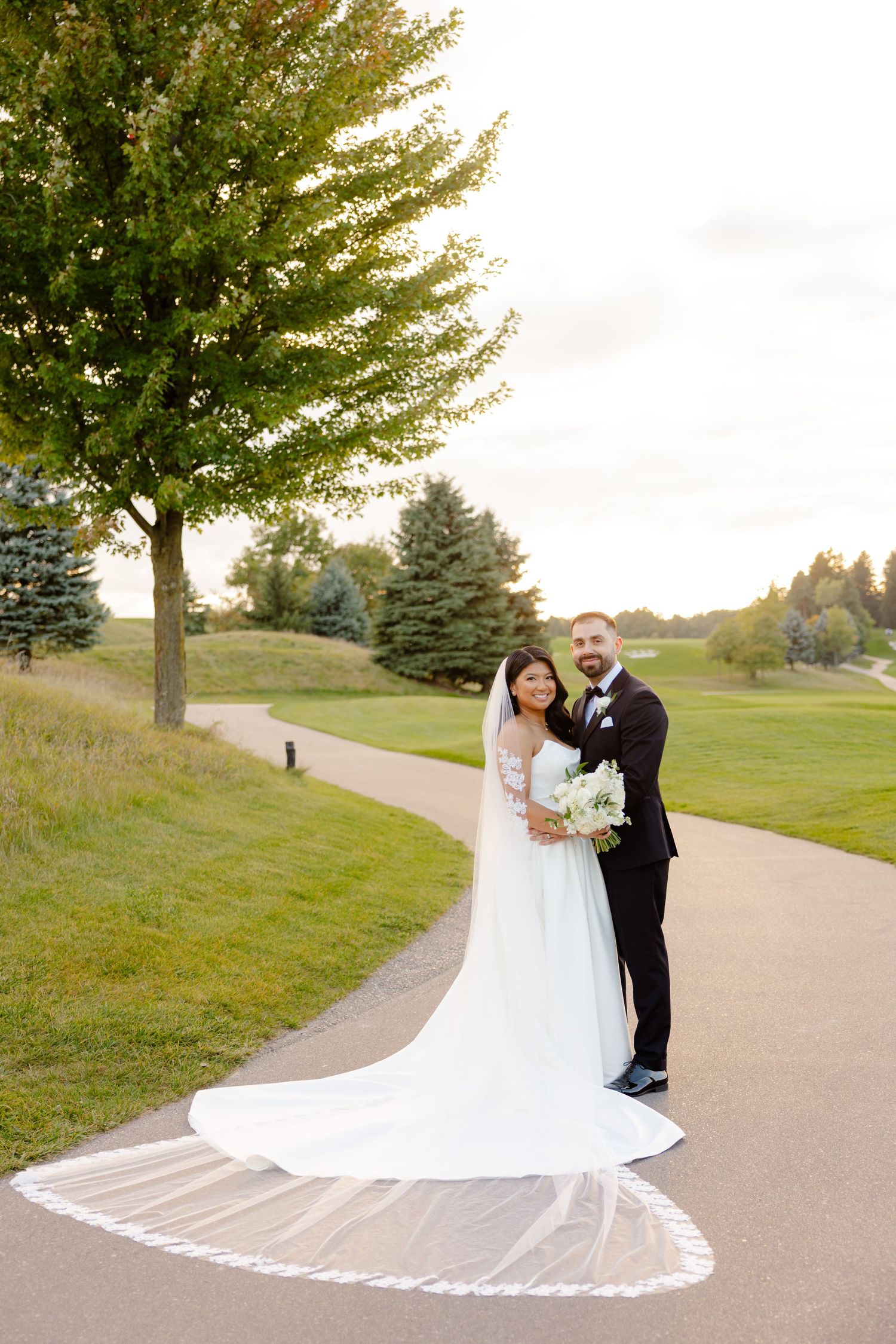 Bride and groom pose on a golf course path with a dramatic cathedral veil spreading behind them.