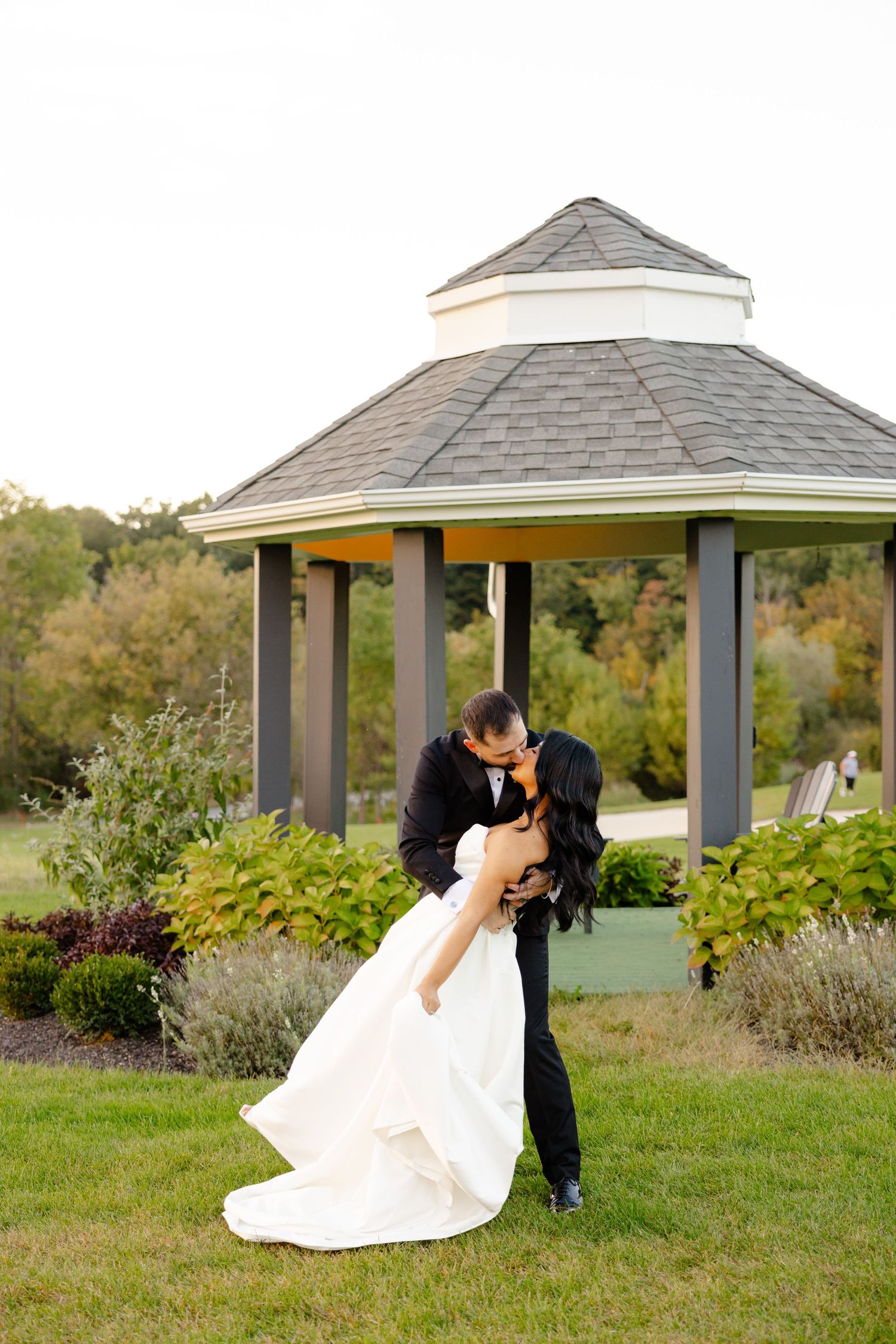 Romantic wedding couple sharing an intimate moment under a garden gazebo surrounded by lush landscaping.