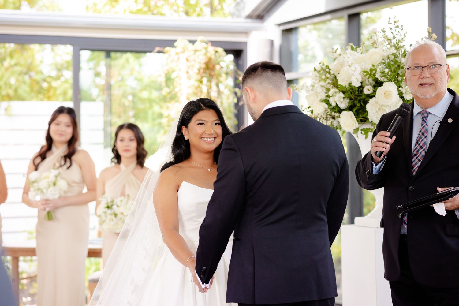 Wedding ceremony in a light-filled venue decorated with white floral arrangements and elegant decor.