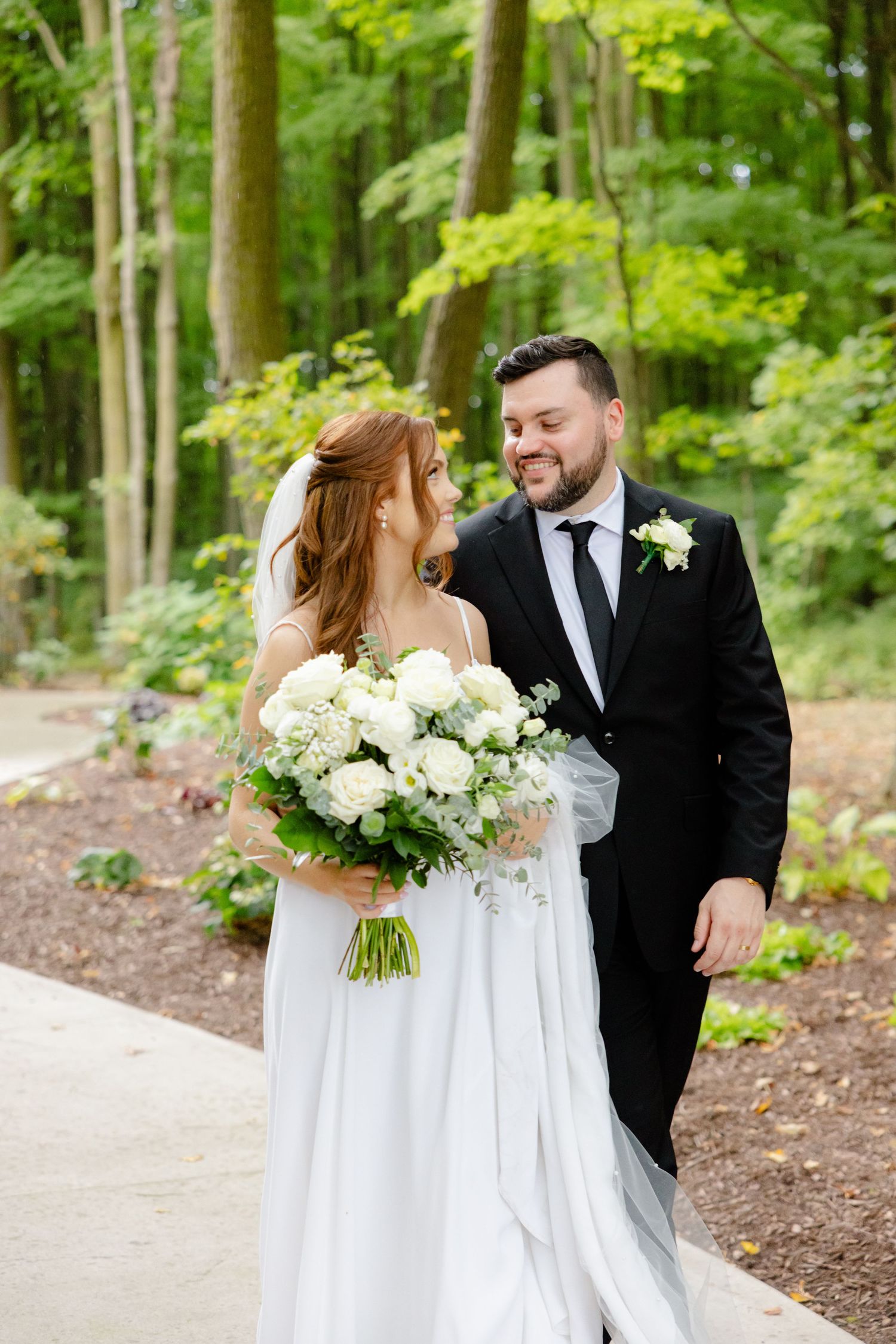 Candid wedding moment captured on garden path with lush forest background.